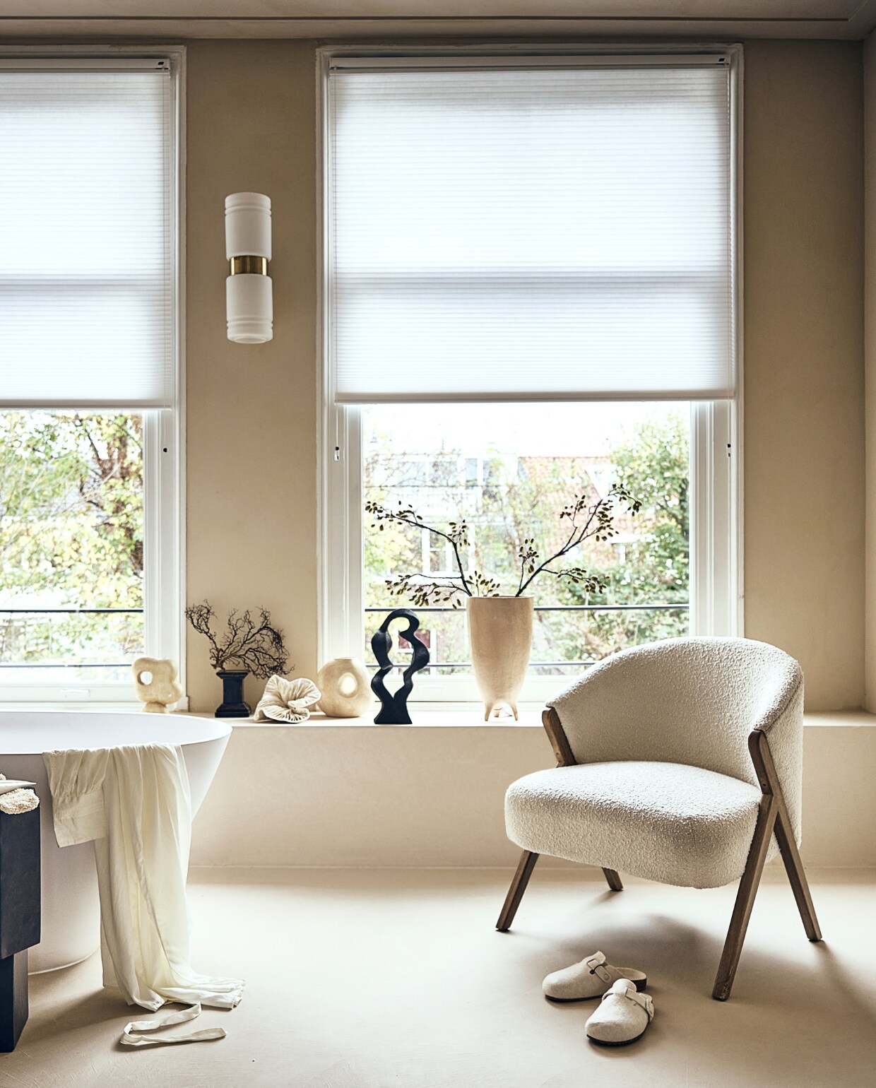 Witte stoel met houten poten en badstof bekleding € 299,-, badmat op rek € 19,99, handcrème € 15,99, vloerkleed € 219,-, sloffen € 25,99, beige bakje met deksel € 17,99, ochtendjas € 69,99, scrubhandschoen op zwart kastje, prijs op aanvraag (zarahome.com). Zwart rek van Ferm Living € 189,- (vtwonen.nl). Beige plaid € 99,-, vaasje met rond gat links € 54,95, beige vaas in het midden € 57,95, zwarte siervorm € 79,95, grote beige vaas € 89,95, borstel € 15,95 (eijerkamp.nl). Kunstwerk aan wand, prijs op aanvraag (@ansdekruyf). Papieren kunstwerk € 150,- (elsavisser.com). Zeep in fles € 18,-, losse zeep € 22,-, zeepfles op zwarte kruk, prijs op aanvraag (sukha.nl). Zwarte natuurvorm € 35,- (taxidermy.nl). Zwarte schaal op drie poten € 19,99 (hm.com). Zwarte kruk € 249,-(aedamanthony.nl). Muurverf onbekend. Overig privébezit. vtwonen 01-2023 | styling liza wassenaar | fotografie sjoerd eickmans