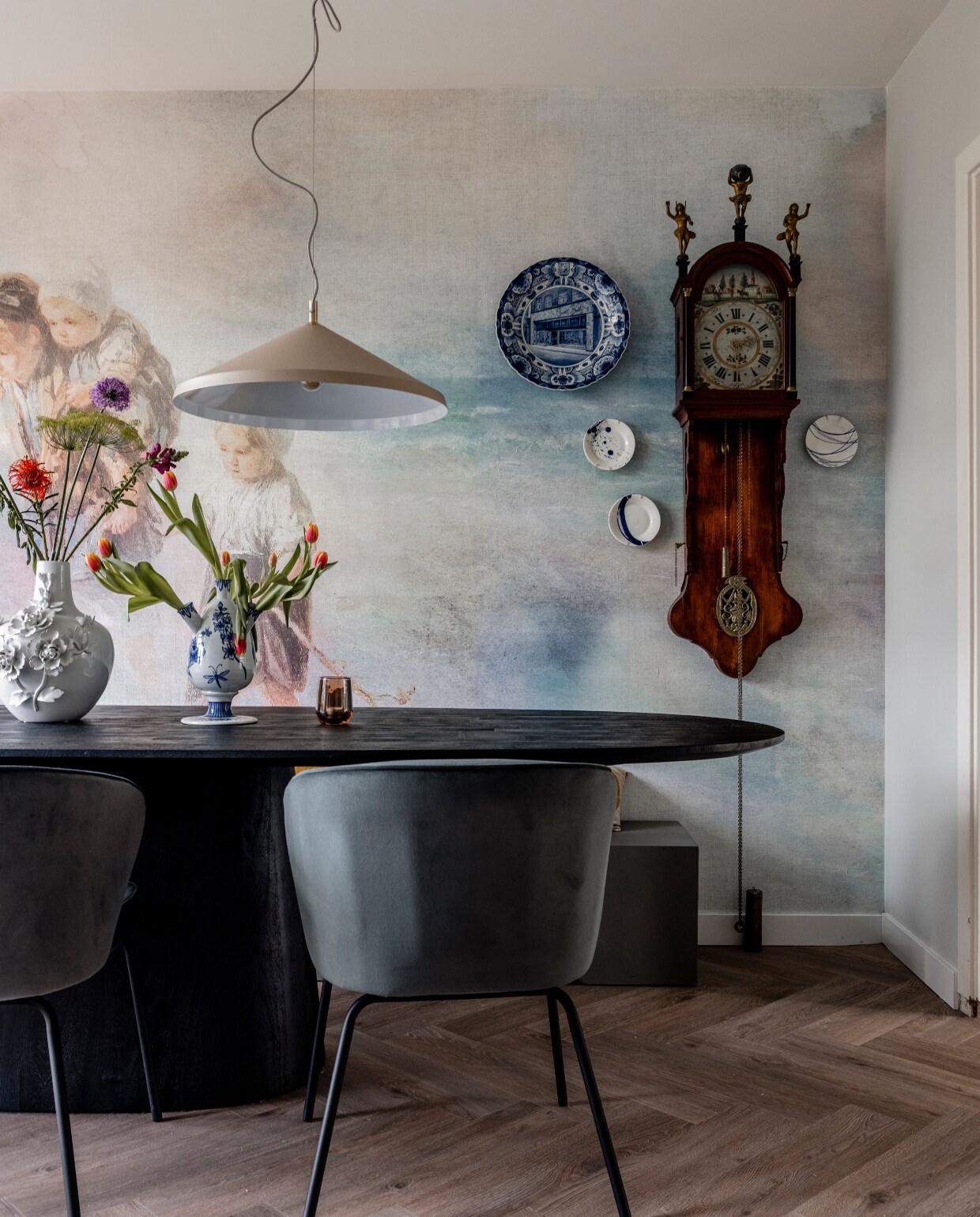 Flexa Creations muurverf extra mat Misted Grey (flexa.nl). Behang met kinderen Masterpiece 358127, behang zonder kinderen Masterpiece 358126 (eijffinger.com). Vloer Galtymore Oak 86851 met vloerverwarming van Warp Systems (aanhuis.nl). Eettafel Aron, eetkamerstoelen Admit, bank Ceme, hanglampen Montreux (eijerkamp.nl). Zitkussen in Sand (nahka.nl). Witte vaas 3D Rose van Polspotten, tulpenvaas Anouk Tulp van &amp;k Amsterdam, gebaksborden aan wand Pacific van Royal Doulton (vtwonen.nl/shop). Overig privébezit. vtwonen 06-2023 | afl. 8 Voorburg seizoen 18| fotografie Sonja Velda | styling Frans Uyterlinde