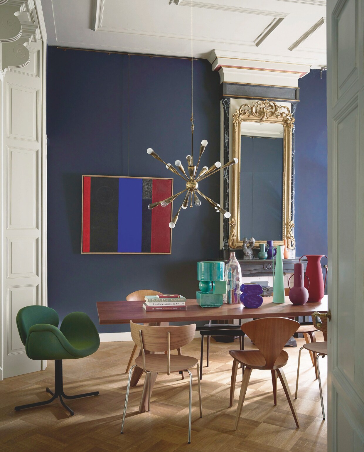 Muurverf Drawing Room Blue 253 van Farrow &amp; Ball (vestingh.nl). Vintage notenhouten eettafel van Jean Prouvé voor Vitra, 220x90x75 cm (lxbxh) € 2500,-, groene eetkamerstoel van Pierre Paulin voor Artifort € 650,-, vintage spoetniklamp € 500,-, vintage Norman Cherner eetkamerstoelen in walnoot € 600,-, schilderij van Joop Vreugdenhil (@iconic_objects). Eetkamerstoel van Ferm Living € 345,-, metalen vazenset van Polspotten € 180,-, ornament op schouw van Ferm Living € 144,99 (vtwonen.nl). Hoge keramische vintage flesvaas € 245,- (bestwelhip.nl). Keramisch object in zeegroen van Inge Simonis € 850,- (ingesimonis.nl). Blauwe vaas € 35,- (klevering.com).  Overig privébezit. vtwonen 11-2024 | styling Cleo Scheulderman | fotografie Jeroen van der Spek