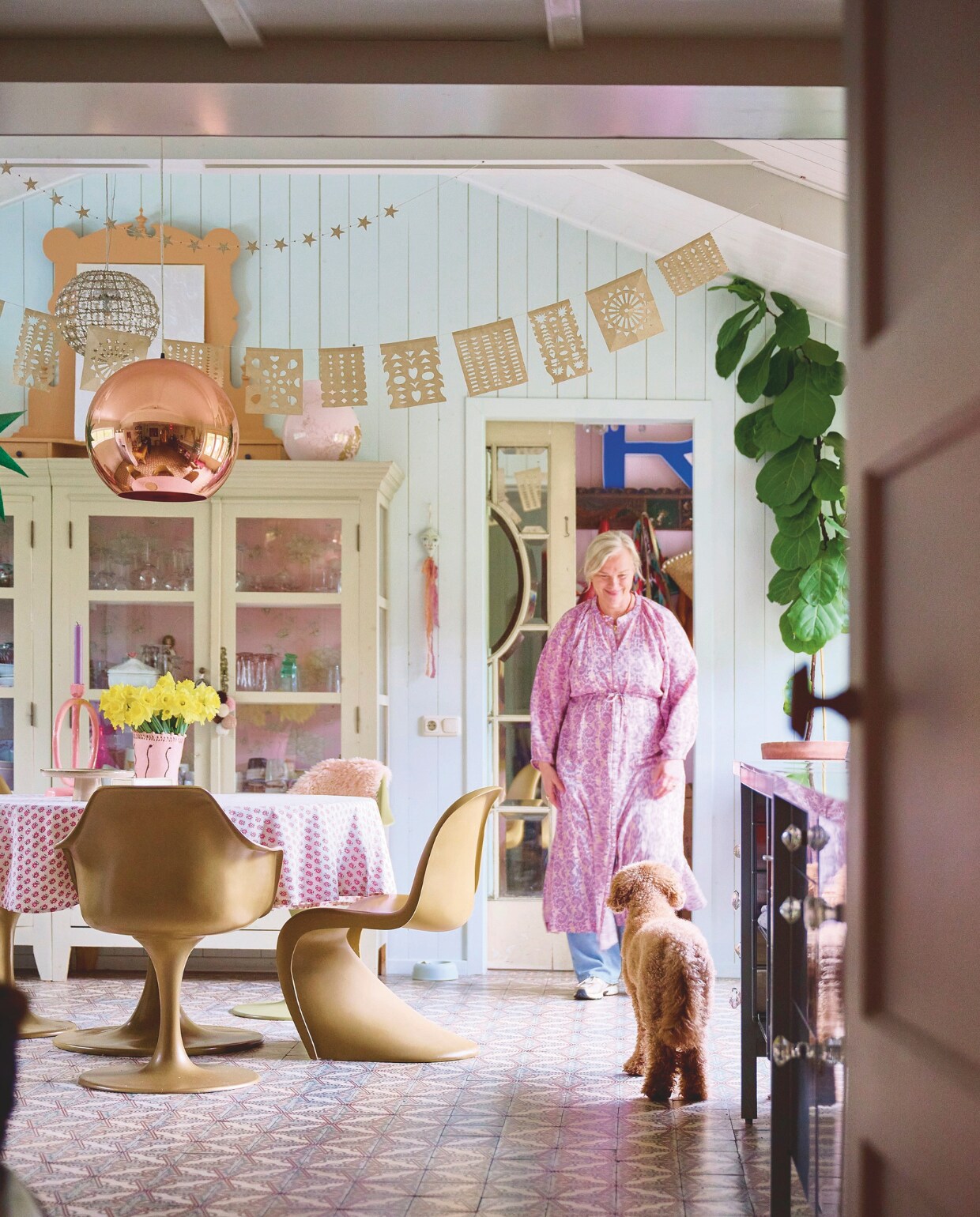 Muurkleur Pavilion Blue van Farrow &amp; Ball, tegelvloer Jan van IJken, keuken Ikea, aanrechtblad lokale keukenhandelaar, servieskast Opsetims, eettafel en stoelen Household Hardware. Tafelkleed, hanglamp achter de koperen lamp, kaars en glazen Sissy-Boy. Sterrenslinger White cube, Mexicaanse slinger Sukha, kandelaar Junoon by Janice, vaas The English Boys, taartschaal Kwantum, vaas op kast Ikea, hangpop Skippy Cotton, plant en pot tuincentrum. vtwonen 10-2024 | styling Liza Wassenaar | fotografie Sjoerd Eickmans