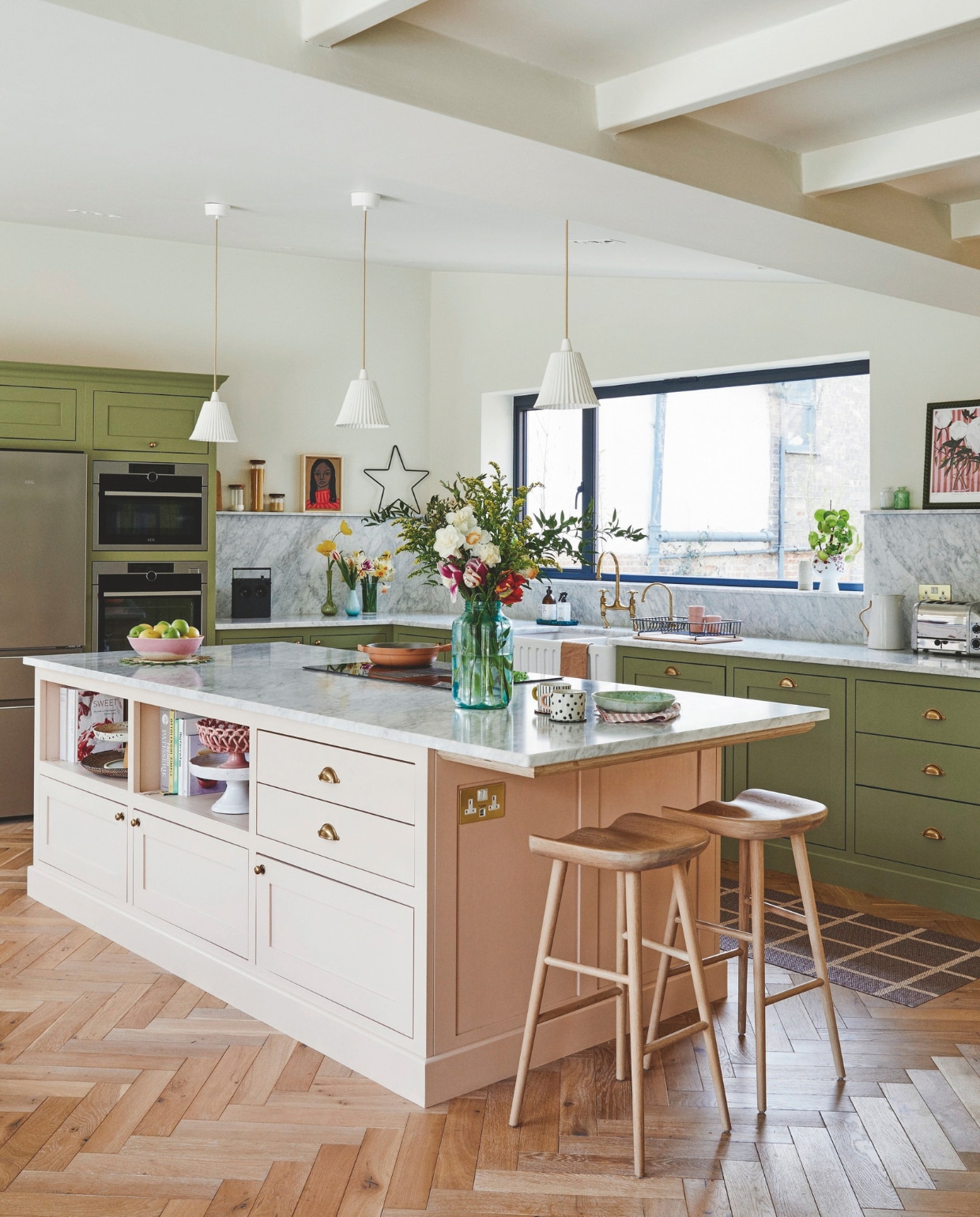 Op maat gemaakte keuken geverfd in Olive en Potted Shrimp van Farrow &amp; Ball, messing handgrepen en kranen Devol,krukken Neptune, ovens en koelkast Aeg, schilderij Rusty Studio, loper Pappelina, roze fruitschaal Vanil, muurverf Clunch van Farrow &amp; Ball. vtwonen 11-2024 | styling Kay Prestney | fotografie Brent Darby