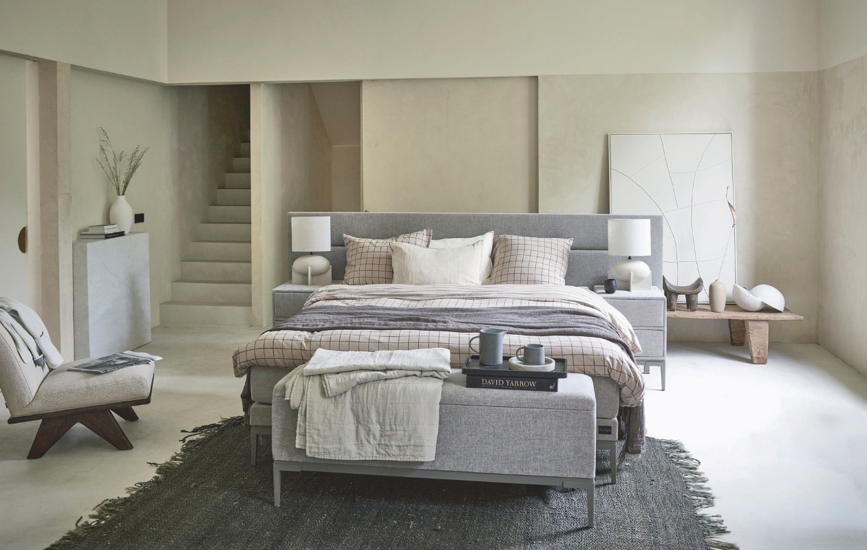 Boxspring Lifestyle by vtwonen Cinnamon Large, vanaf 140x200 cm € 2090,-, nachtkastje Cardemom met twee lades, 45x45x62 cm (lxbxh) vanaf € 199,-, voetenbank Clove 140x33x57 cm (lxbxh) vanaf € 339,-. Hier uitgevoerd in stof Mirage Taupe, met metalen frame in kleur Champagne en poot Track. vtwonen 11-2024 | styling Sanne Ketelaar, Cleo Scheulderman | fotografie Peggy Janssen, Jeroen van der Spek