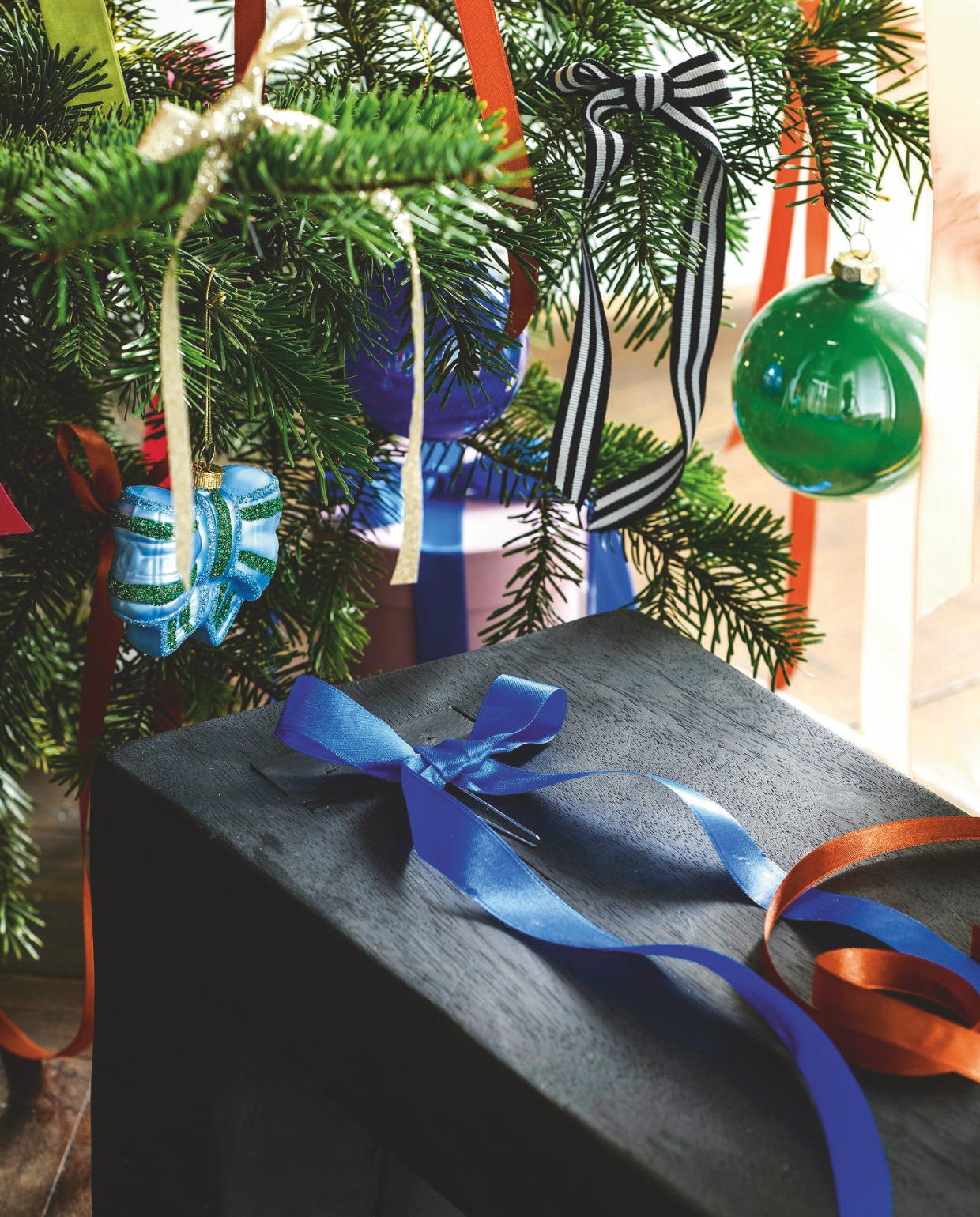 Natuurlijke kerstboom Nordmann, 240 cm (h) € 55,- (buitengoeddeboomgaard.nl). Roze-rode en blauw-groene glazen strikken € 14,95 (klevering.com). Effen glazen ballen in blauw, groen, roze en lila van House of Seasons, set van 4 € xxxx (vtwonen.nl/shop). Satijnen lint, vanaf van 8 meter per rol € 3,29 (pipoos.nl). Overig privébezit. vtwonen 12-2024 | styling Marit Saladini | fotografie Louis Lemaire