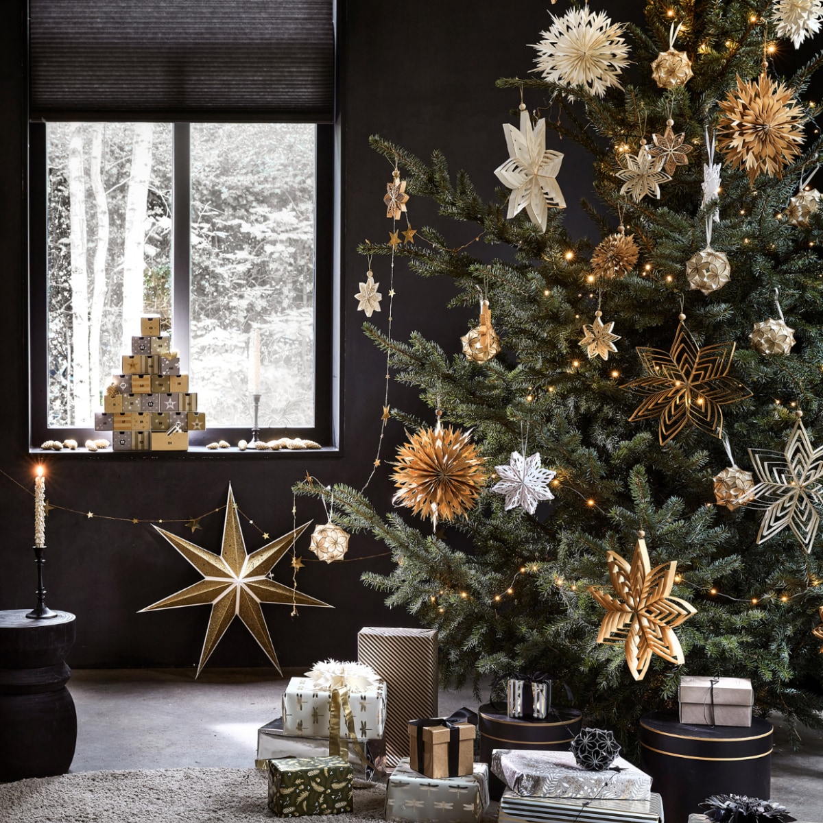 Kartonnen adventskalender € 27,99, goudkleurige kaars met glitter, per 2 € 6,99, goudkleurige papieren ster, 70x19 cm (Øxd) € 9,99, goudkleurige slinger met sterren, 210 cm (l) € 3,49 (ook verkrijgbaar in zilver). In de boom: diverse papieren ornamenten in de kleuren goud, wit, zilver en zwart, per stuk vanaf € 2,49, zilverkleurige lichtslinger warm wit met 30 ledlampjes op batterijen inclusief display en timer, 300 cm (l) € 3,99. M.m.v. karwei.nl (zwarte kandelaar, taupe schapenvacht, zwarte houten kruk Bikkel, taupe schapenvacht), hema.nl (inpakpapier), janvanvulpenboomkwekerij.nl (kerstboom). vtwonen 12-2022 | productie Tanja Saarberg, Isa Hoevens | styling Kim van Rossenberg | fotografie Peggy Janssen