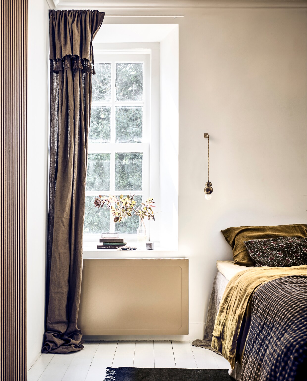 Radiatorbekleding voor plaatradiator, uitvoering classic in kleur Ral 1019 grijsbeige, prijs is afhankelijk van afmeting (sentimo.nl). Bruine gordijnen met kwastjes, 130x300 cm set van 2 € 99,- (hm.com). Groen kussensloop met bloemendessin, 40x60 cm € 29,99, glazen opbergkist € 19,99, linnen bedsprei, 230x250 cm € 159,-, vierkante zwarte schaal € 17,99 (zarahome.com). Linnen kussensloop Moutarde, 50x70 cm € 35,-, linnen dekbedovertrek Moutarde, 140x200 cm € 129,- (thearchivestore.com). Hoeslaken kleur Bosco, 160x200 cm € 55,- (midnatthome.com). Messing lamp Ball Light Bracket van Michael Anastassiades € 938,- (justhaasnoot.nl). Overig privébezit. vtwonen 11-2022 | styling Kim van Rossenberg | fotografie Sjoerd Eickmans | uitvoering Richard van Meerveld