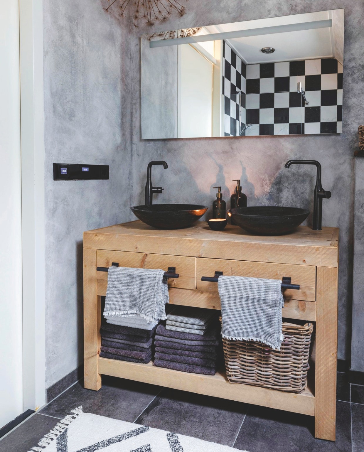 De badkamer met een badmeubel dat Richard en Hilda zelf hebben ontworpen en gemaakt. De waskommen zijn van het merk Plieger. De kranen van Solar Nederland. De badmat is gekocht bij Loods 5. De muren zijn behandeld met betonlook verf, de vloertegels komen van Boer Staphorst. vtwonen landelijk 07-2024 | Styling Rust &amp; tiek | Fotografie Corine Hoge Bavel-Jansen
