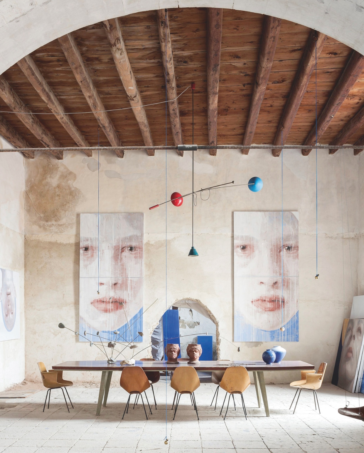 Aan de muur van de studio hangen schilderijen Gemelli van Sergio Fiorentino. Vintage tafel uit de jaren 60.  Stoelen Medea van Vittorio Nobili, vazen van Sergio Fiorentino voor Rometti, de hoofden zijn Caltagirone-keramiek van begin 20ste eeuw. stijlvol wonen 07-2024 | fotografie en tekst Filippo Bamberghi/Living Inside