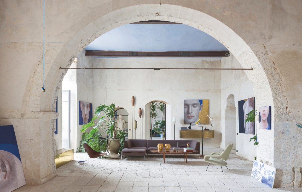 Bank Charles van B&amp;B Italia, rechts een fauteuil van Gastone Rinaldi voor Rima, jaren 60-bijzettafel met daarop antieke Caltagirone-hoofden en vazen van Sabatini. Rechts van de bank een vloerlamp van Stilnovo, achter de bank een lamp van Arredoluce, beide uit de jaren 50. stijlvol wonen 07-2024 | fotografie en tekst Filippo Bamberghi/Living Inside