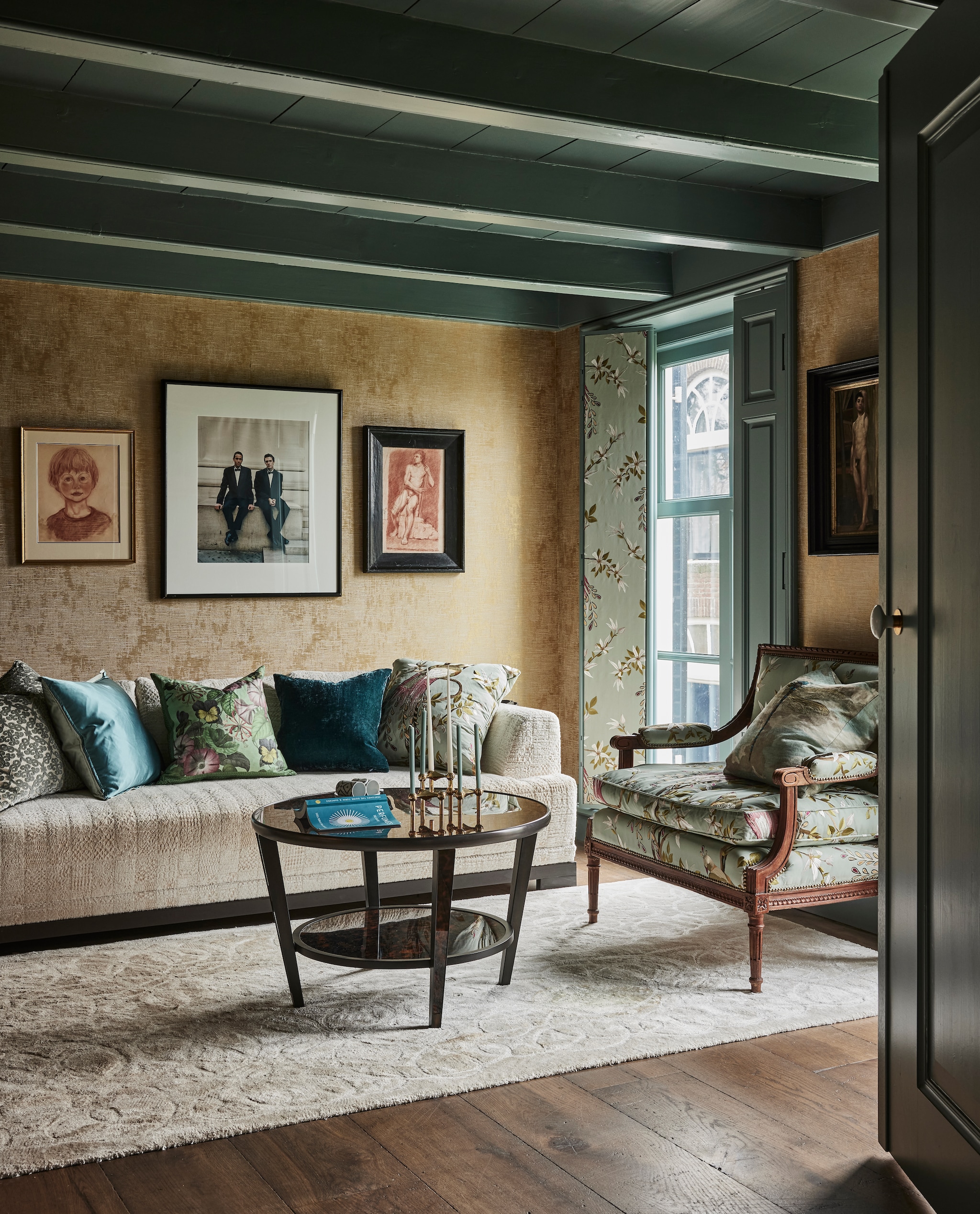 Luiken en fauteuil bekleed met stof Paradiso van Nina Campbell via Osborne &amp; Little. Salontafel Arno Tortoiseshell van William Yeoward. Vloerkleed en kussens Designers Guild via Wilhelmine van Aerssen Agenturen. Bank Canapé California in stof Baalbec Nobilis. Kaarsenstandaard Stoff Nagel. Houten vloerdelen van Landgoed Twickel. Kunst v.l.n.r. schets van Joris als kind, foto onbekend, studieschets. Kleur houtwerk Kerkgrijs Midden van Vettewinkel. vtwonen landelijk 01-2025 | styling Marianne Luning | fotografie Alexander van Berg | tekst Merel van der Lande