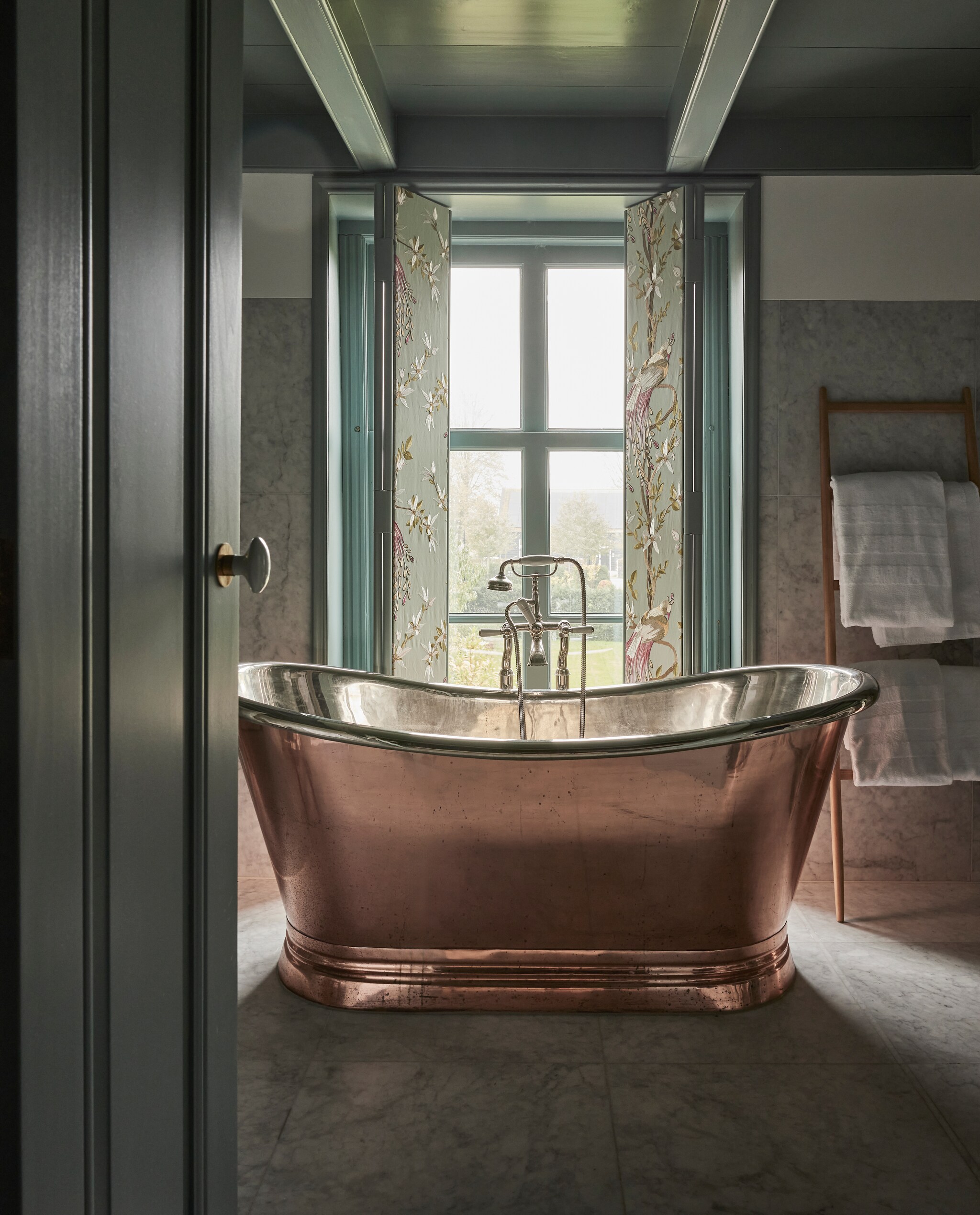 Koper-nikkel bad, vergelijkbare bij Windsor Bathrooms. Handdoekenrek Zara. Handdoeken Designers Guild. Kranen Kenny &amp; Mason. Stof luiken Paradiso Nina Campbell via Osborne &amp; Little. Kleur houtwerk Kerkgrijs licht en Kerkgrijs Midden van Vettewinkel. Marmeren tegels Amata Carrara. vtwonen landelijk 01-2025 | styling Marianne Luning | fotografie Alexander van Berg | tekst Merel van der Lande