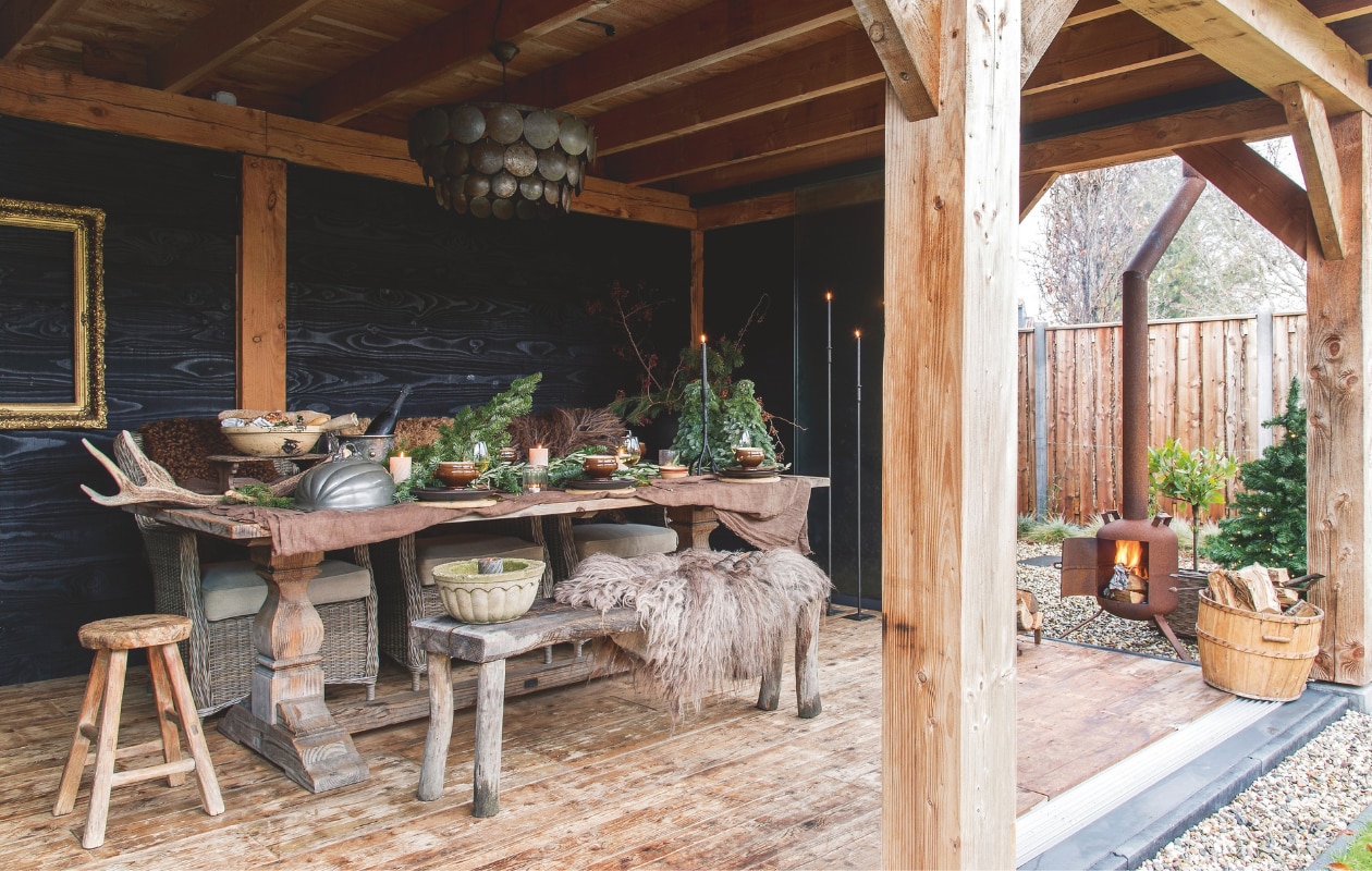 Met kerst tafelen ze urenlang aan de oude kloostertafel onder de veranda. Boven de tafel hangt hanglamp Mura van Hoffz. vtwonen landelijk 07-2024 | styling Peet! | fotografie Joyce Vloet