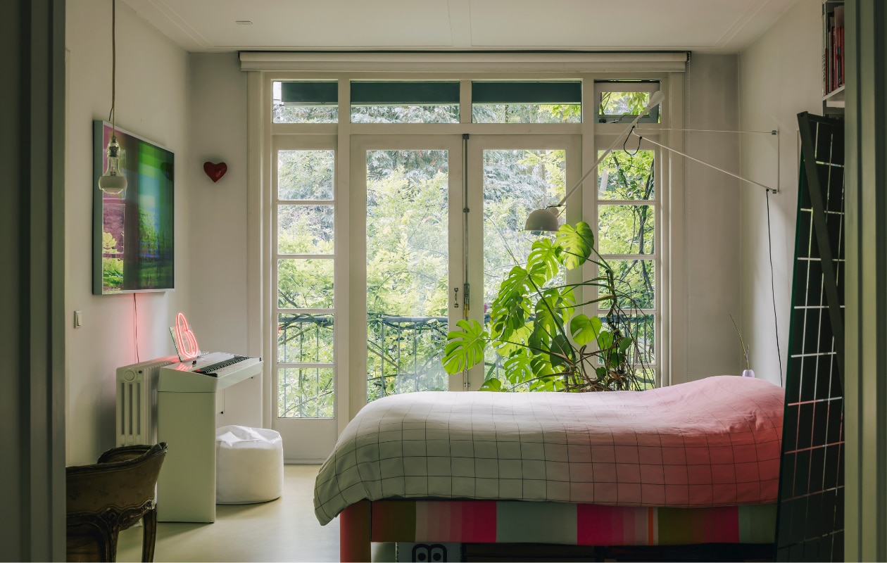 Caroles slaapkamer heeft een balkon met uitzicht op de tuin. De witte wandlamp boven het bed is van Paolo Rizzatto voor Flos, de hanglamp van Ingo Maurer. De hartjes komen van Menno Kroon en de televisie is een speciale uitgave van Samsung. stijlvol wonen 08-2024 | fotografie Katoo Peeters | tekst Tanne Donjacour Gielen