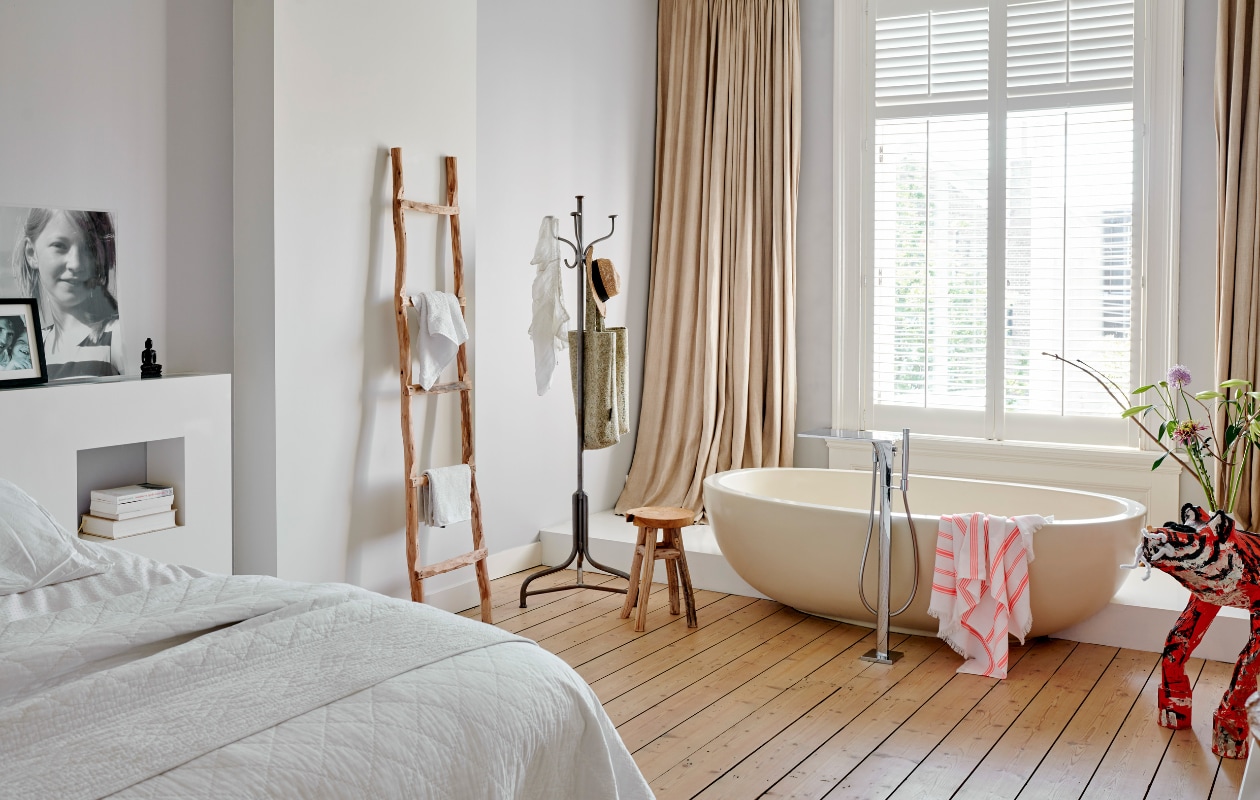 Het bad in de slaapkamer is zo bedacht door de vorige eigenaars. De vloer isgeschilderd met traplak waardoor hij tegen een stootje kan. De linnen gordijnen enshutters werden overgenomen van de vorige bewoners. De tijger van papier-machéis gemaakt door dochter Roos. Ladder van Atelier 8, kapstok en krukje Homestock.Hamamdoek Hema. vtwonen 04-2020 | productie Features &amp; More | styling Wilma Custers | fotografie Renee Frinking