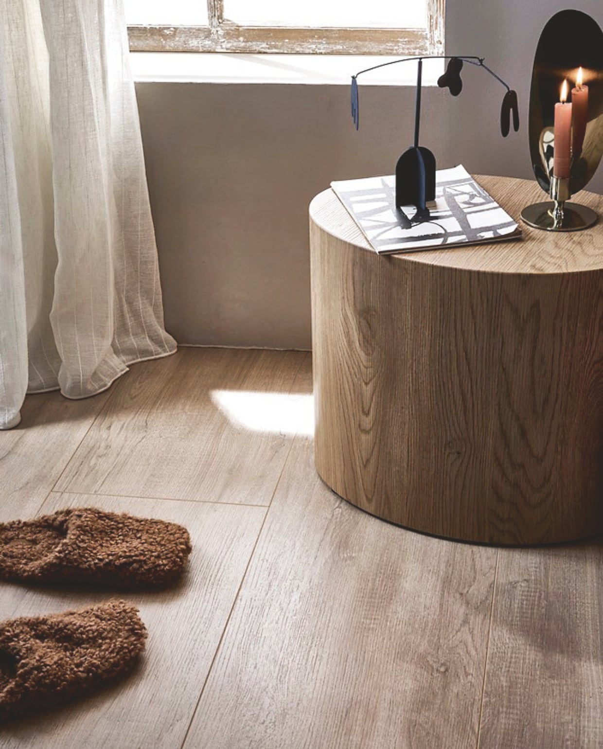 Muurverf krijtmat Warm Grey, 1 liter € 27,99. Laminaatvloer XL in Rafter naturel, met groef, per lamel 138x32,6x0,8 cm (lxbxh), per m² € 32,99. Gordijn op maat Inbetween transparant in stof Wide Stripe, kleur Ecru White Stripe (2316), per meter vanaf € 27,99.M.m.v. vtwonen.nl/shop (bijzettafel Dice van By Fonq), zarahome.com (pantoffels), hm.com (kandelaar, mobile). Overig privébezit. vtwonen 13-2024 | styling Sanne Ketelaar | fotografie Peggy Janssen