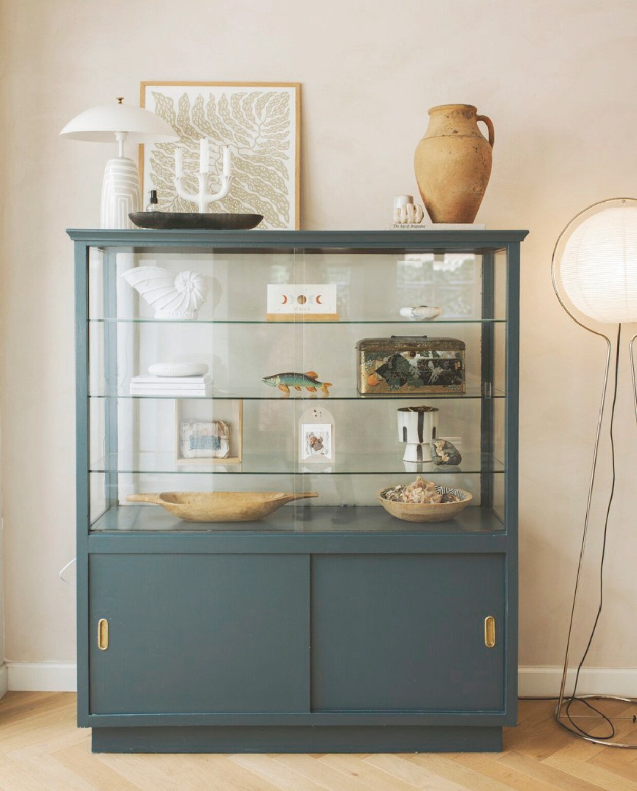 Muurkleur White Truffle van Lab Paint, kleur kast Vintage Blue van Karwei. Staande lamp vintage Ikea. Vitrinekast erfstuk. In de kast: kringloop, erfstukken en tweedehands vondsten. Kruik Marktplaats, kandelaar kringloop, poster The Poster Club, tafellamp zelfgemaakt. vtwonen binnenkijkspecial 11-2024 | fotografie Merel Annabel Visscher