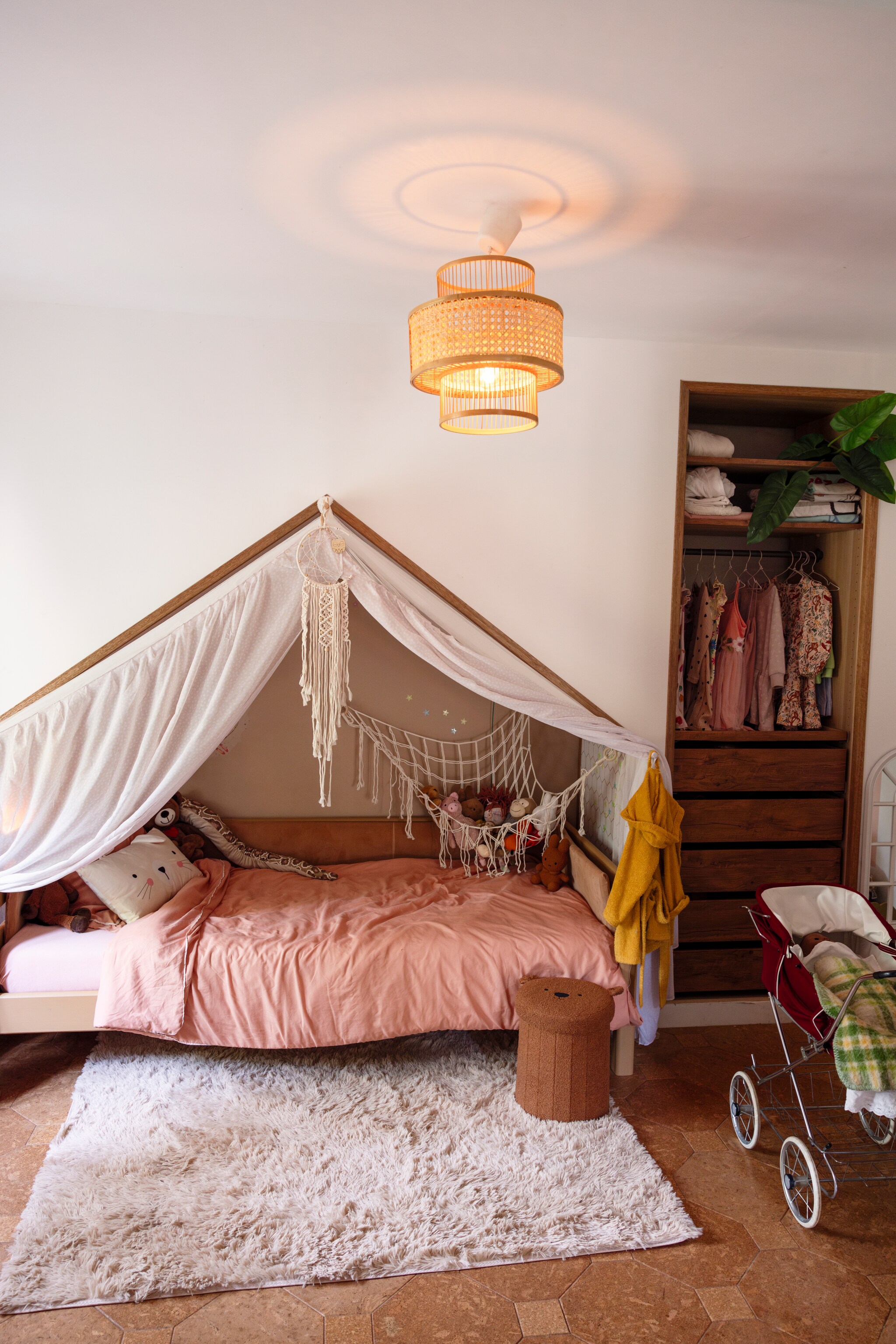 Bed via Marktplaats, daarna zelf aangepast en geverfd en dezelfde bruine kleur als in de huiskamer, gordijn gemaakt door Jannekes moeder. Dromenvanger zelf geknutseld, hangnet Temu. Hanglamp Made, vloerkleed Volero, dekbed Jysk. Kast van Ikea zelf ingebouwd. Opvouwbare opbergpoef Teddy van Action, poppenwagen Marktplaats, vloer kurkvloer.nl. vtwonen 02-2025 | styling Ilona Jongepier | fotografie Dana van Leeuwen | tekst Chris Muyres