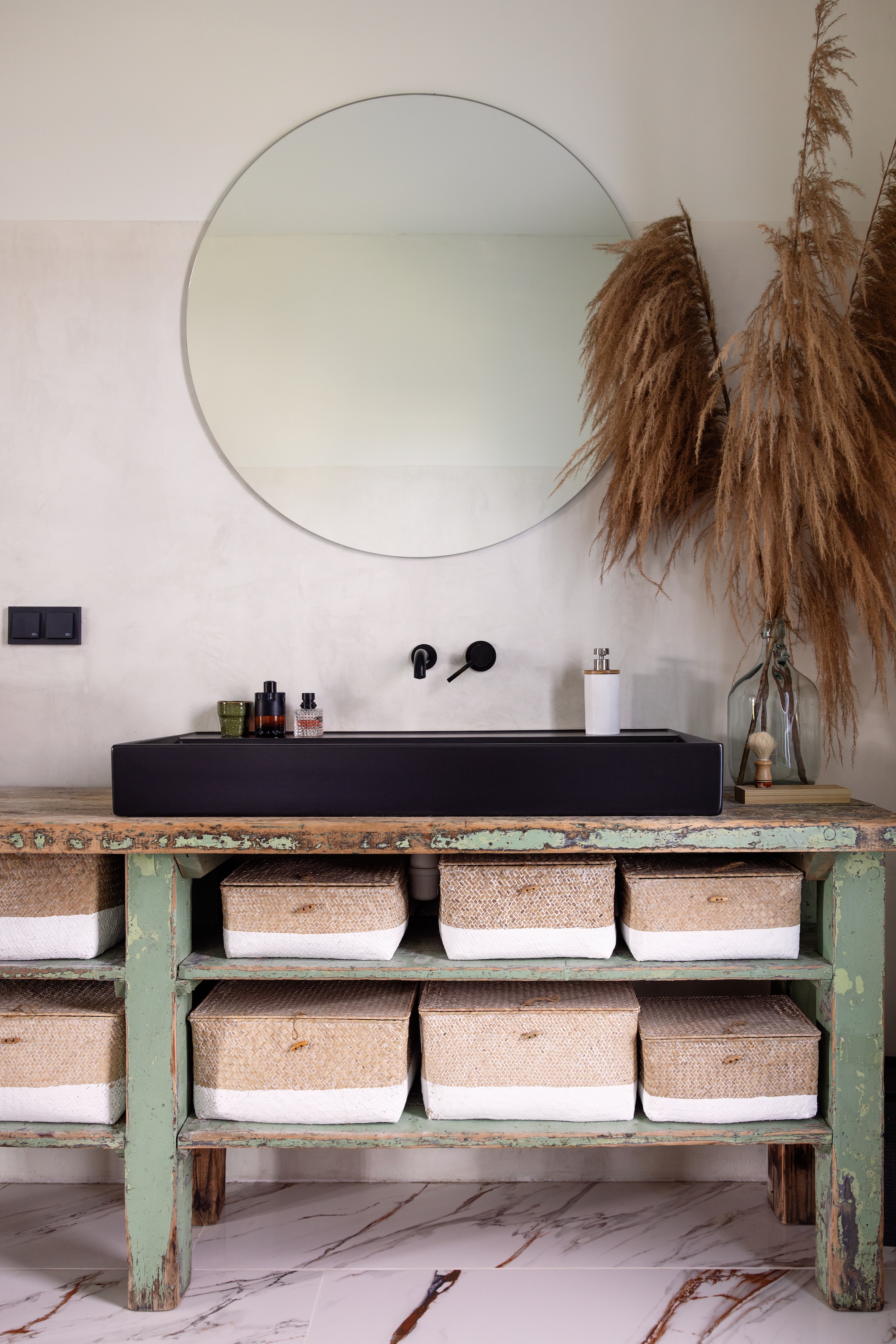 Vloertegels Verona Marmer Tegels in Huis. Muurkleur Beton ciré wit, spiegel Badkamerspiegels. Wastafelmengkraan Study Colors 1 van Tres en wastafel Cloud van BWS via Tegeldepot. Meubel PimsTra Meubelen, zeeppomp Grace van Sealskin, pampastak uit trouwdecor van vriendin, fles Braumarkt, gevlochten manden Maisons du Monde vtwonen 02-2025 | styling ilona jongepier | fotografie dana van leeuwen | tekst Mirjam Rosema-Verhulst