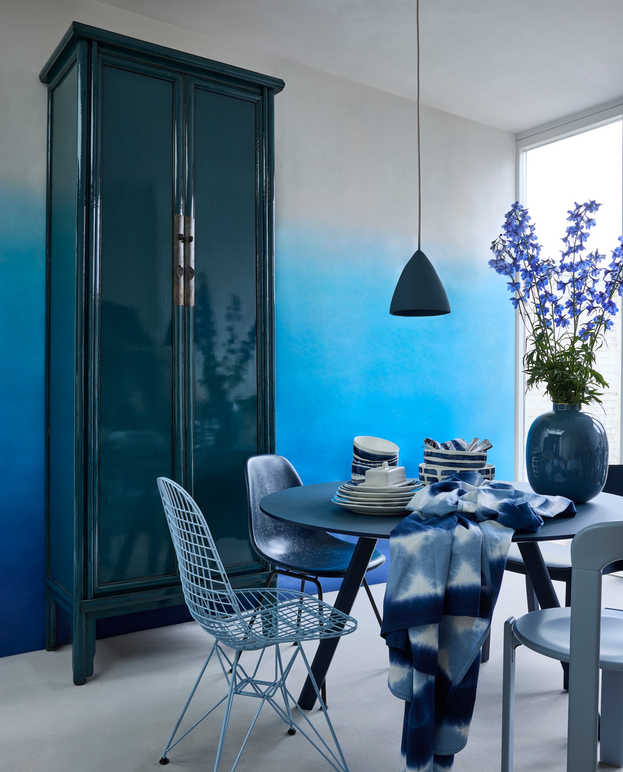 Behang Saraille Cobalt van Designers Guild, 300x45 cm (lxb) per rol € 449,- (wva.nl). Lichtblauwe houten eetkamerstoel Rey, 44x49x80 cm (bxdxh) € 484,-, houten tafel CPH 25, 120x74 cm (Øxh) € 1799,-, en terracotta botervloot Barro € 39,- (hay.com). Houten kast Bayan, 90x50x240 cm (bxdxh) € 1695,- (hetkabinet.nl). Stalen draadstoel Eames, 49x51x85 cm (bxdxh) € 500,- en fiberglass eetkamerstoel Eames van Vitra 46,5x55x83 cm (bxdxh) € 680,- (loods5.nl). Terracotta hanglamp Nasser € 45,- (householdhardware.nl) geverfd in krijtverf 52 Kerkdal, 100 ml € 9,95 (lauthentique.nl). Katoenen tafelkleed, 150x250 cm € 59,95, katoenen servetten, set van 2 € 12,95 en porseleinen servies Tie-Dye van vtwonen: borden vanaf € 7,95, kommen € 12,95 en schalen vanaf € 29,95. Metalen vaas Pip Studio € 59,95 (shop.vtwonen.nl). Rvs bestekset Carum, 4-delig € 25,45 (nordal.com). vtwonen 4-2025 | styling Marianne Luning | fotografie Alexander van Berge