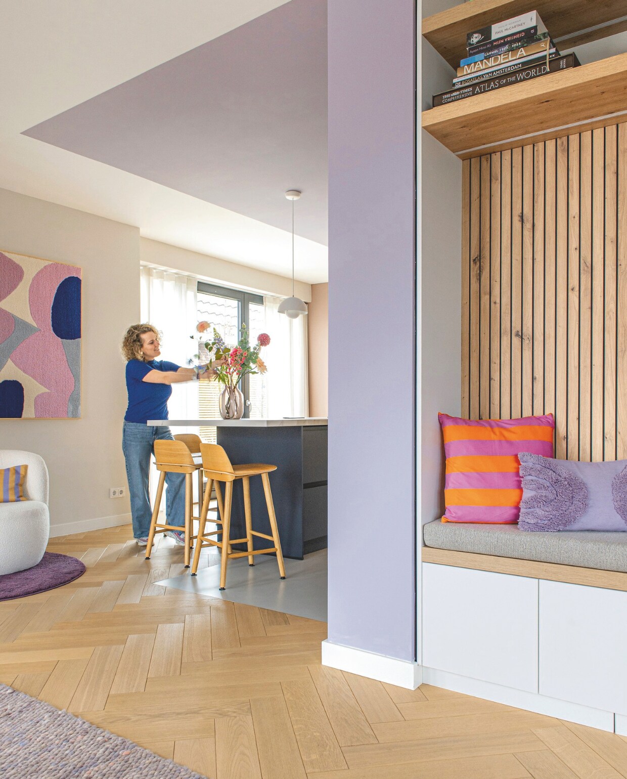 Kunstwerk Studio Mirte. Witte fauteuil, kussen Fést. Paars kleed Ikea. Hanglamp Verner Panton, &amp;Tradition. Barkrukken Muuto. Vaas Loods 5. Nis met bank maatwerk van Tritop Interieurbouw. Kussens: lila Blokker, gestreept Xenos. vtwonen binnenkijkspecial 11-2024 | styling jeske weel | fotografie caroline coehorst