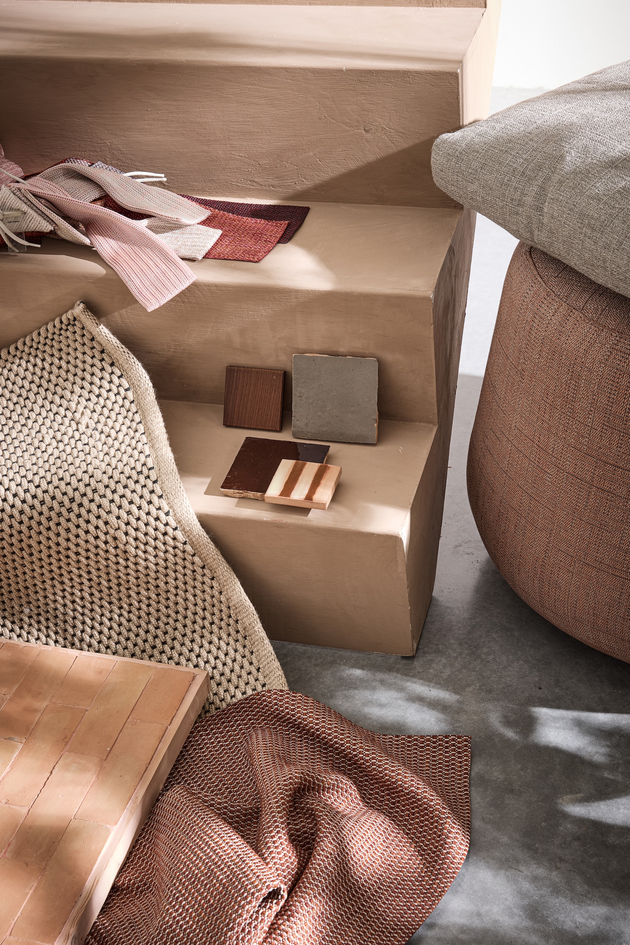 Vloerkleed Brink &amp; Campman, prijs op aanvraag (vloerkledenwinkel.nl). Polyolefine stofstalenset Chain outdoor en Rope, houten staal  Aurea Le232 en gestreepte tegel Segni Pml126 van Paola Lenti, terracotta stofstaal, kussen en poef Fat-Sofa Outdoor van B&amp;B Italia vanaf € 884,- (dacks.nl). Terracotta tegels met roze voegsel en grijze en bruine tegels Zelliges, per m² € 115,- (householdhardware.nl). vtwonen 02-2025 | styling marlies does | fotografie peggy janssen