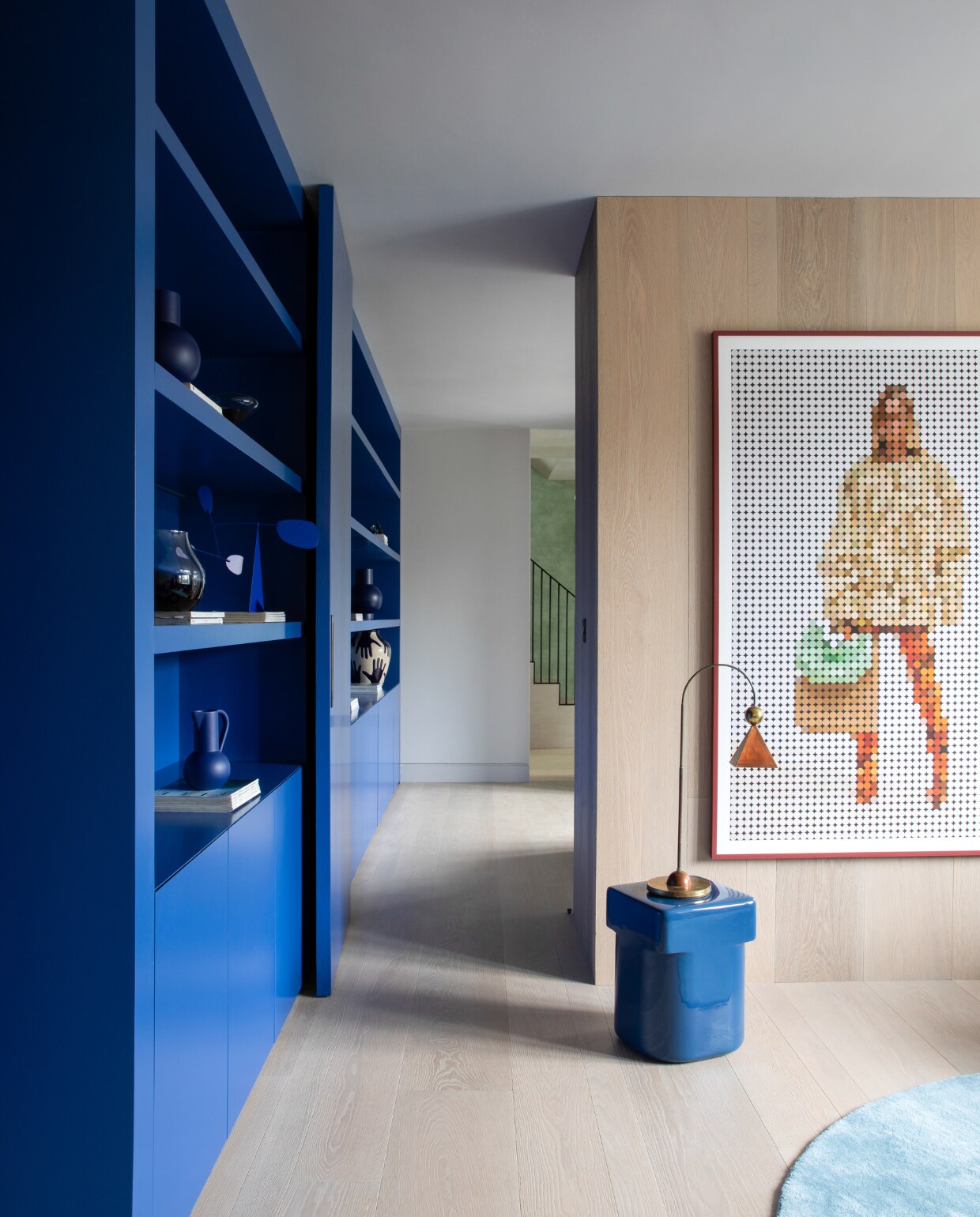De blauwe kasten en de houten vloer van Trunk Flooring verbinden de muziekkamer en biobliotheek. Kunstwerk There’s Someone I Forgot To Be van Elsbeth Shaw. Bijzettafel Landmark van Dan Schofield voor Nine, wandlampen Kin van Sazerac Stitches, vloerkleed Rugvista. stijlvol wonen 01-2025 | productie Living Inside | fotografie Ruth Maria Murphy