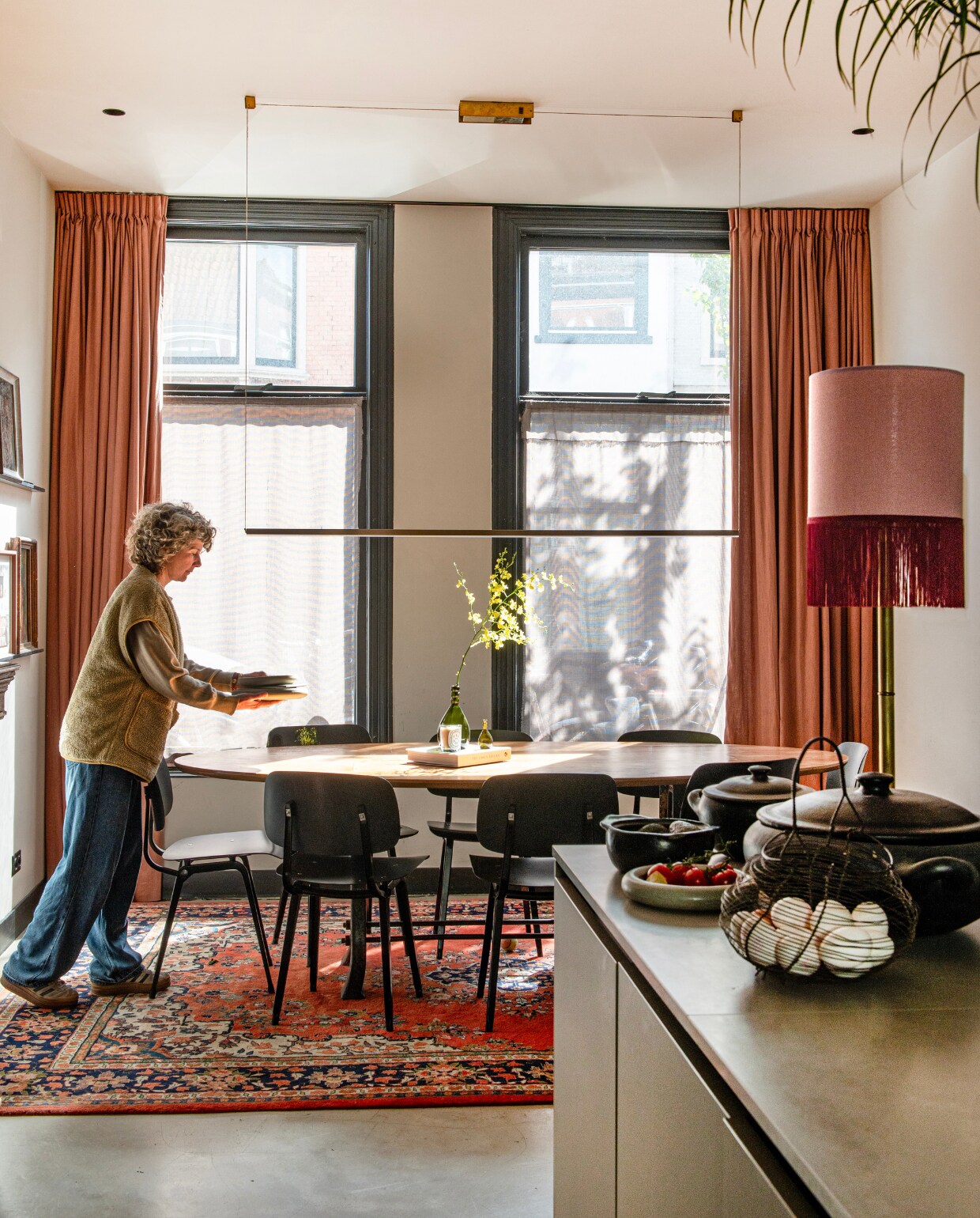 Schemerlamp Madame Garage, eiermand kringloop, zwarte potten en pannen uit Brazilië, hanglamp Piet Hein Eek, tafel uit kringloopwinkel voorzien van gerecyclede fineerlaag door Combitex, stoelen Revolt van Friso Kramer heruitgebracht door Hay, Perzisch tapijt Rozenkelim, gordijnen Karwei. vtwonen 01-2025 | productie De Binnenkijkers | fotografie Caroline Coehorst