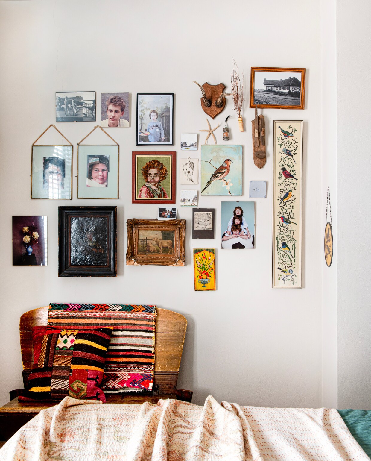 Kussen en doek meegenomen uit Turkije. Houten bank kringloopwinkel Emmaus Fenix, aan de muur werkjes met een persoonlijke waarde. vtwonen 01-2025 | productie De Binnenkijkers | fotografie Caroline Coehorst