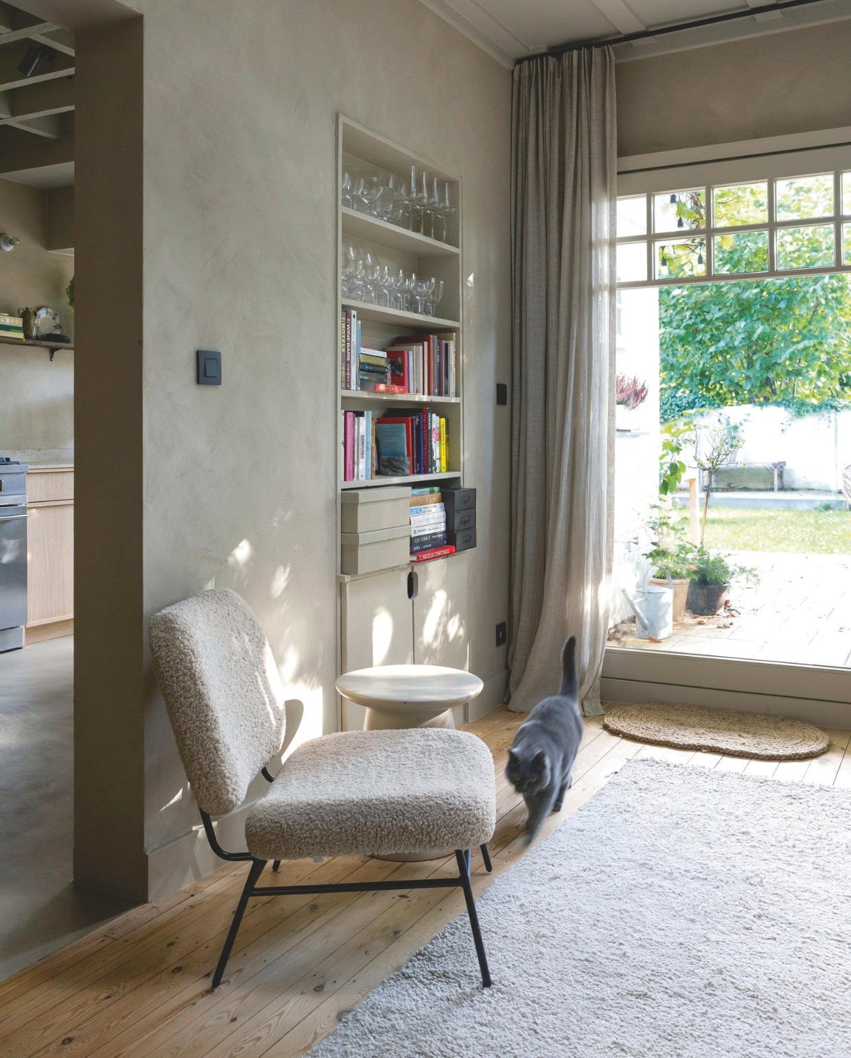 De kalkstuc op de muur geeft een warm fluwelig effect, mooi in combinatie met de met bouclé stof beklede stoel. Een ondiepe nis biedt plaats aan onder andere mooi glaswerk. vtwonen landelijk 01-2025 | fotografie Sarah van Hove
