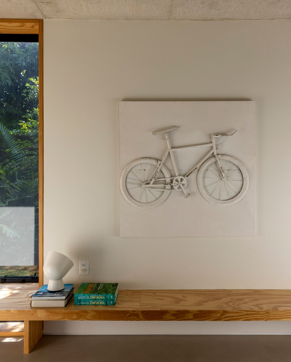 Houten bank Marcenaria Lunas. Lamp Ikea. Kunstwerk gemaakt door Breno van een witgeschilderde fiets. vtwonen 01-2025 | styling Simone Raitzik | fotografie Andre Nazareth