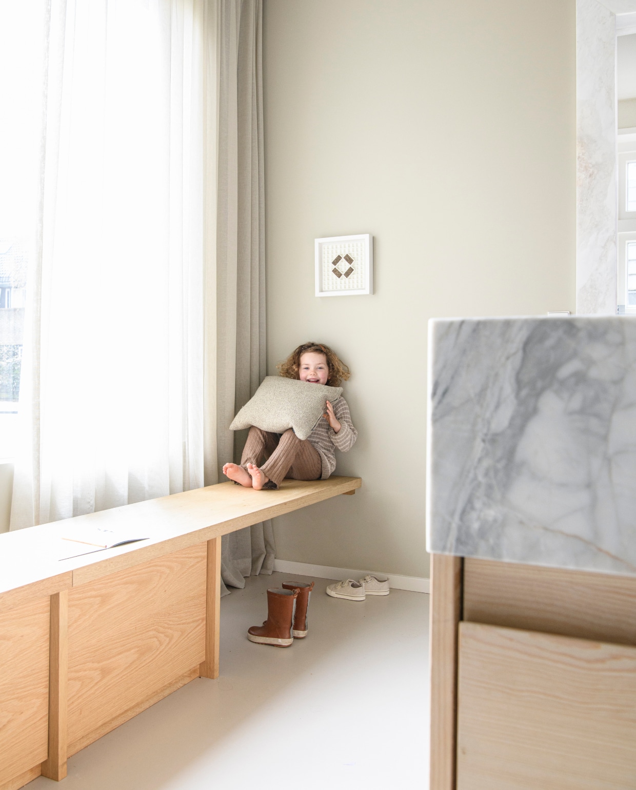 Dochter Nina zit op een op maat gemaakte bank van eikenhout. Kunstwerk erboven Different Choice van Rob van Hemert. vtwonen 01-2025 | styling Esther Loonstijn | fotografie Louis Lemaire