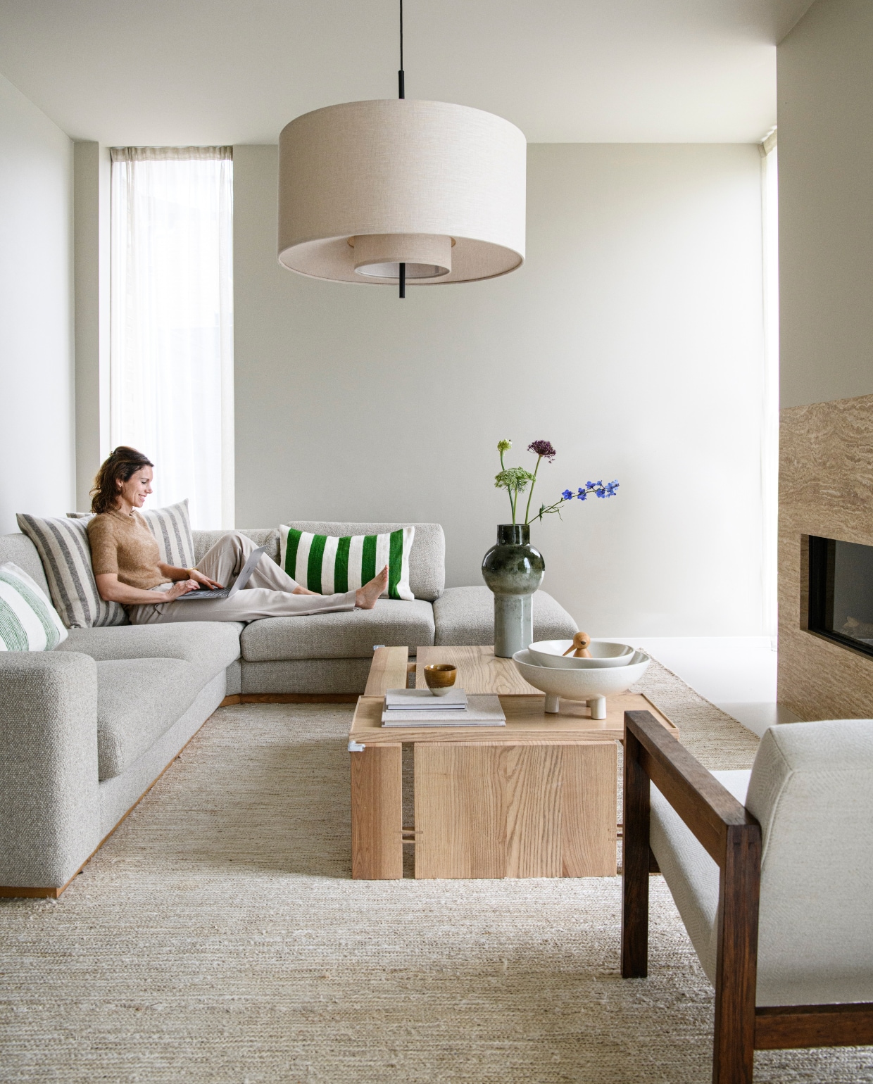 Lyan in de zithoek in de aanbouw achter in het huis. Zitbank Sepia in stof Monza van Bolia, kussens Household Hardware. De salontafel is een ontwerp van Avenue Design Studio. Vloerkleed Nuna van Casa Gitane, haard met travertin van SolidNature, hanglamp Margin van New Works, vintage fauteuil Spectrum. vtwonen 01-2025 | styling Esther Loonstijn | fotografie Louis Lemaire