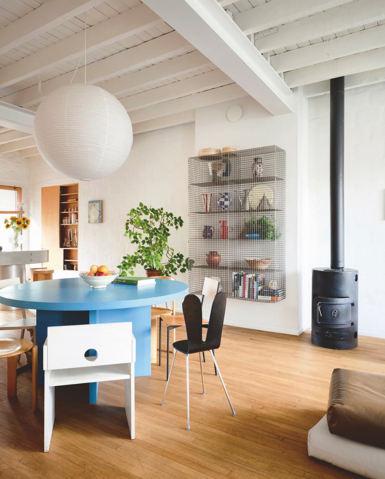 De woonkamer op de eerste verdieping. De tafel van gelakt mdf is een eigen ontwerp, eromheen staan twee stoelen chair.01 van Vormen, twee vintage Bruno Rey stoelen, Sanaa Armless Chair van Maruni, Alu Chair van Muller Van Severen en een witte tweedehands stoel. In de kast Wire C #1, ook van Muller Van Severen, staan vintage- en rommelmarkt vondsten. Hanglamp Paper van Hay. stijlvol wonen 02-2025 | productie Living Inside | fotografie Mr. Frank