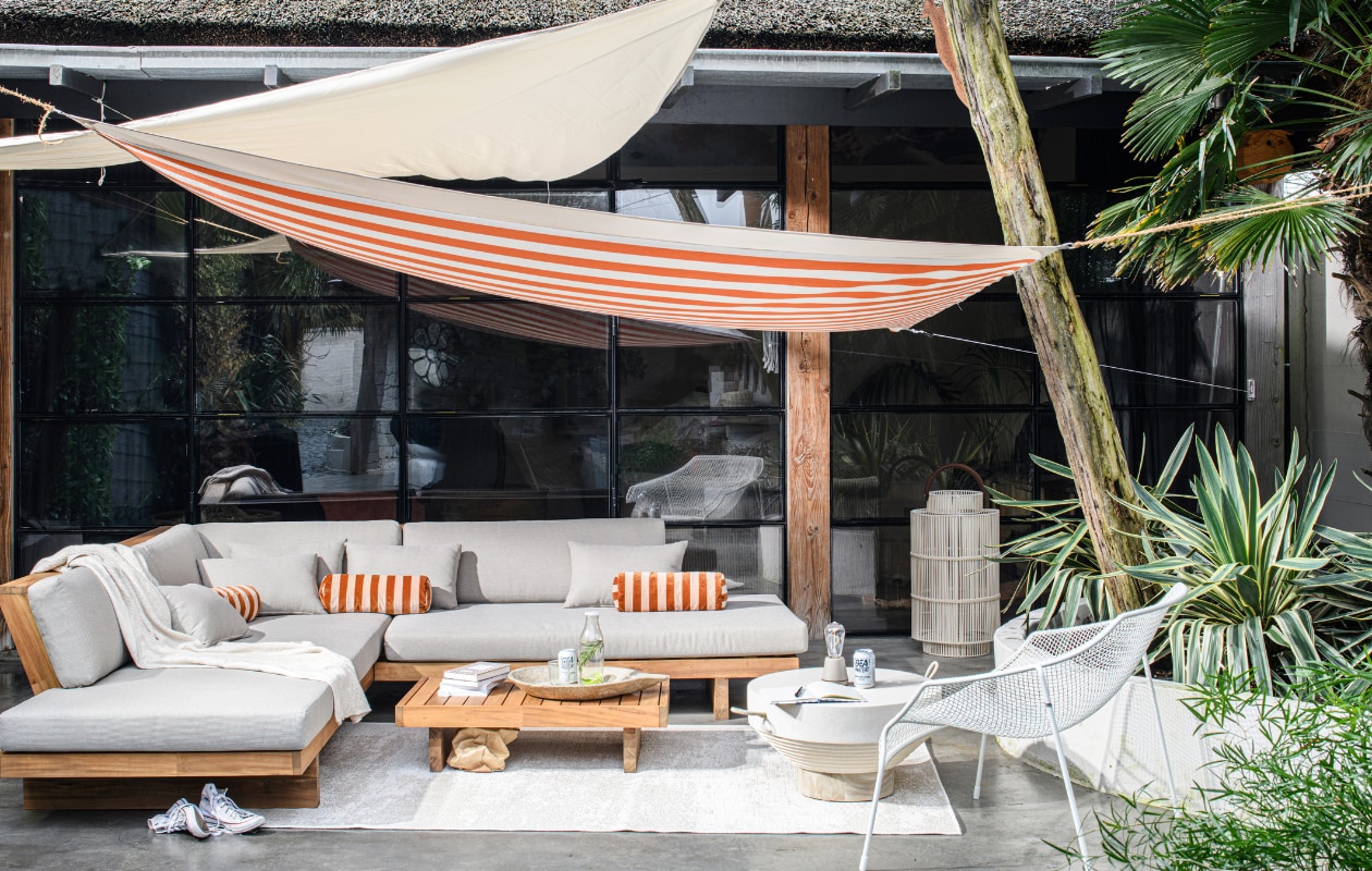 Acaciahouten loungeset van Nous Garden, 269x269x70 cm (bxdxh) € 1999,-, binnen- en buitenkleed van Nous Living, gerecycled pet, 230x160 cm € 89,99 (wehkamp.nl). Plaid Pergamon in wafelstructuur, katoen en wol, 130x170 cm € 199,-, outdoor salontafel Jimbaran, glasvezel en teakhout, 80 cm (Ø) € 899,-, outdoor lantaarn Bartolome XL, kunststof, glas, metaal € 399,- (rivieramaison.com). Gestreepte katoenvelours rolkussenhoes Bolster € 94,- (christinalundsteen.com). Marmeren schaal € 165,- (rawmaterials.eu). Gepoedercoat stalen loungestoel Heaven € 654,- (emu.it). Notitieboek € 5,- (flyingtiger.nl). Glazen fles € 2,95, glas, gerecycled glas  € 4,95 (dille-kamille.nl). Oranje-wit gestreepte outdoor stof Dralon, waterafstotend acryl met teflonlaag, stofbreedte 160 cm, per meter € 22,65 (stoffamstueck.de). Schaduwdoek Hold-An, uv-beschermd polyester, 300x300 cm € 30,-, driehoekig schaduwdoek Hold-An, 300x300 cm € 11,- (jysk.nl). vtwonen tuin special 10 | styling Marit Saladini | fotografie Louis Lemaire | assistentie Rosa van Schie en Kiki de Koning