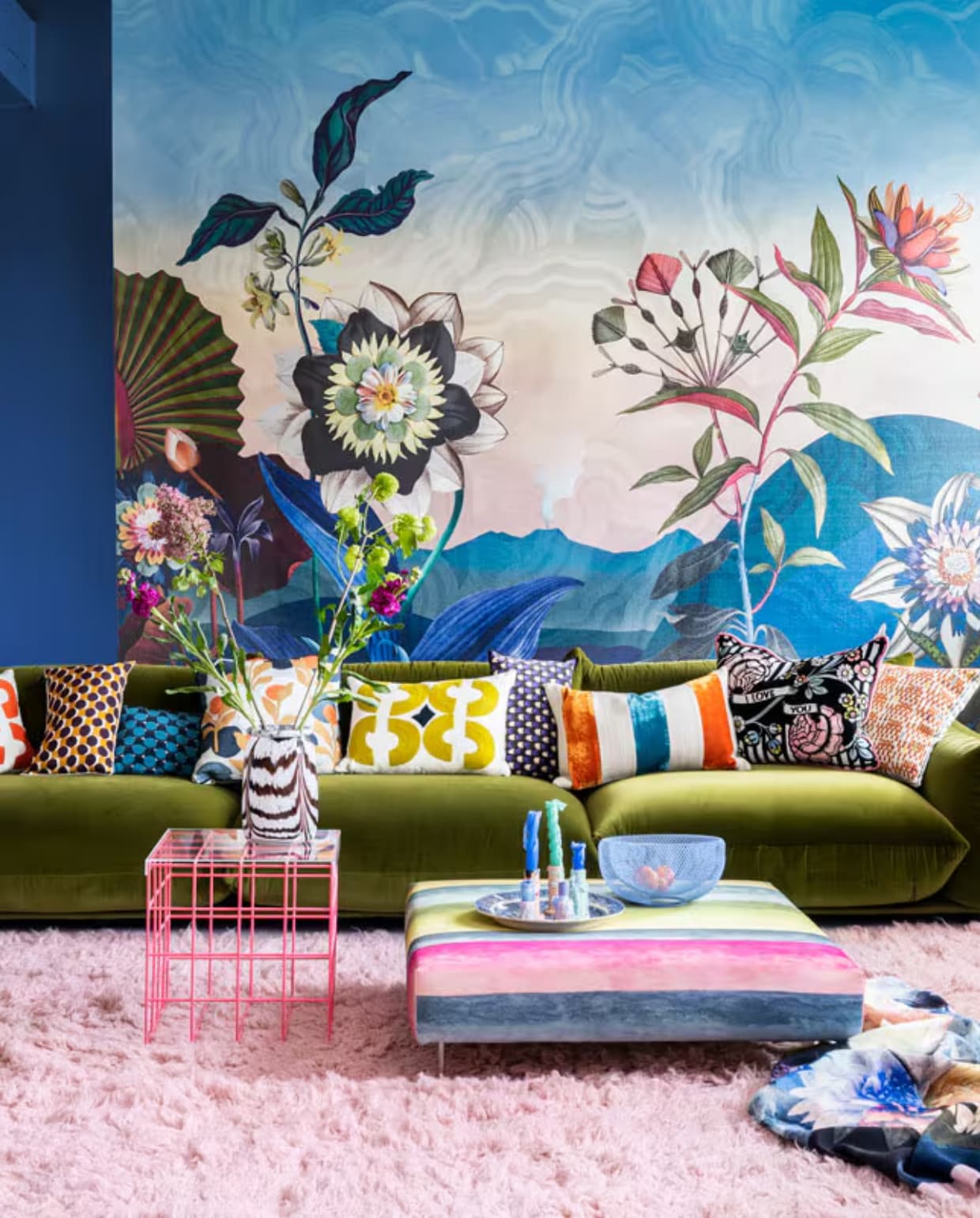 Paneel met behang Atlantis Aube van Christian Lacroix voor Designers Guild, 300×350 cm € 927,- (wva.nl). Blauwe muurverf Exciting Night No. 96 van Lab Paint, per liter € 45,- (vestingh.nl). Groene velours bank van Arflex, 96x354x70 cm (dxbxh) € 5709,-, roze fauteuil van Warm Nordic, 95x84x80 cm (lxbxh) € 2190,-, zachtroze hoogpolig wollen vloerkleed van Layered, 250×350 cm € 1090,- (goeds.nl). Multikleurige voetstoel in stof Rayure Chinoise Alchemilla van Designers Guild, 90×90 cm € 1485,-, oorfauteuil Harper Chair bekleed met stoffen van Christian Lacroix voor Designers Guild € 3220,- (wva.nl). Verstelbare vloerlamp € 659,- (hay.nl). Roze staaldraad tafel van Bold Monkey, 41x41x40 cm (lxbxh) € 165,- (boldmonkey.com). Kandelaars vanaf € 14,50, kaarsen van Hay, per 6 € 25,- (vtwonen.be). Glazen vaas € 85,- (hay.nl). Vintage bord € 25,- (hetgroteavontuur.nl). Blauwe gaasschaal € 39,- (festamsterdam.com). Kussens van links naar rechts: rood geborduurd € 149,-, langwerpig model van zijde, per stuk € 89,- met bloemdessin € 109,-, groen geborduurd € 149,-, alles van Lelievre (loggerewilpower.com), velours streep van William Yeoward € 121,-, bloemen Christian Lacroix voor Designers Guild € 192,-, geborduurd € 132,-, wollen plaid van Designers Guild € 327,- (wva.nl). vtwonen