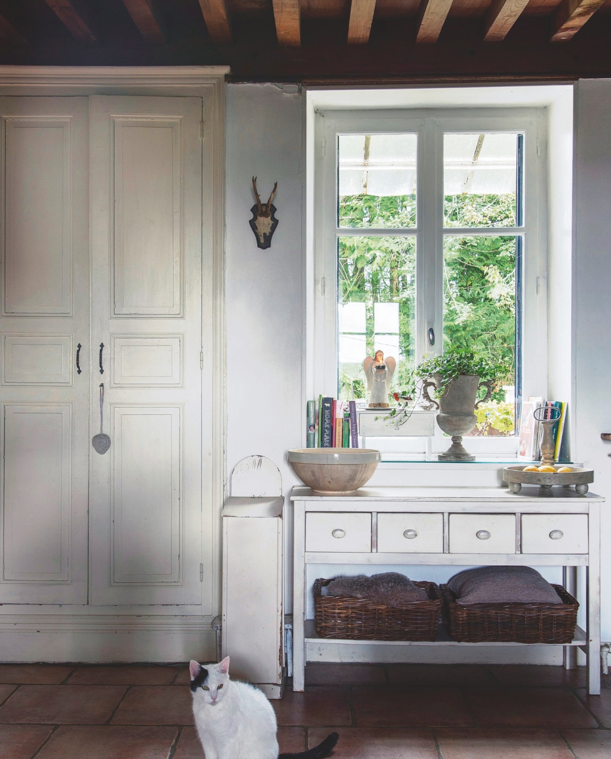 De crèmekleurige kast zit ingebouwd in de muur, iets wat je in oude Franse huizen vaker tegenkomt. Dankzij de dikke muren is de binnenkant heerlijk koel: het meubel deed vroeger dan ook dienst als koele bergruimte. Links naast de sidetable staat een stokbroodkastje met een klep. Hierin werden de stokbroden vers gehouden. vtwonen Landelijk 2-2025 | styling Peet Styling! | fotografie Joyce Vloet | tekst Marie Masureel