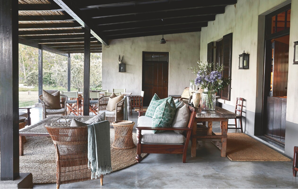 Ook vanaf deze diepe veranda is het uitzicht eindeloos. Een groot rond vloerkleed verwarmt het gepolijste beton, terwijl dekens, plaids en kussens op de royale banken en versleten leren fauteuils voor ultiem comfort zorgen op frisse avonden. Bank en tafel vintage. Soortgelijke poef en plaids Benuta, vloerkleed Westwing. vtwonen landelijk 02-2025 | Styling Luanne Toms | Fotografie Elsa Young | Tekstbewerking Mirjam Rosema-Verhulst