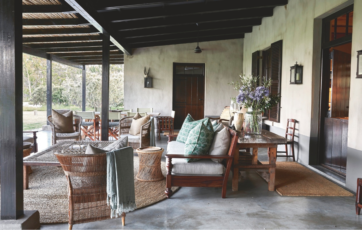 Ook vanaf deze diepe veranda is het uitzicht eindeloos. Een groot rond vloerkleed verwarmt het gepolijste beton, terwijl dekens, plaids en kussens op de royale banken en versleten leren fauteuils voor ultiem comfort zorgen op frisse avonden. Bank en tafel vintage. Soortgelijke poef en plaids Benuta, vloerkleed Westwing. vtwonen landelijk 02-2025 | Styling Luanne Toms | Fotografie Elsa Young | Tekstbewerking Mirjam Rosema-Verhulst