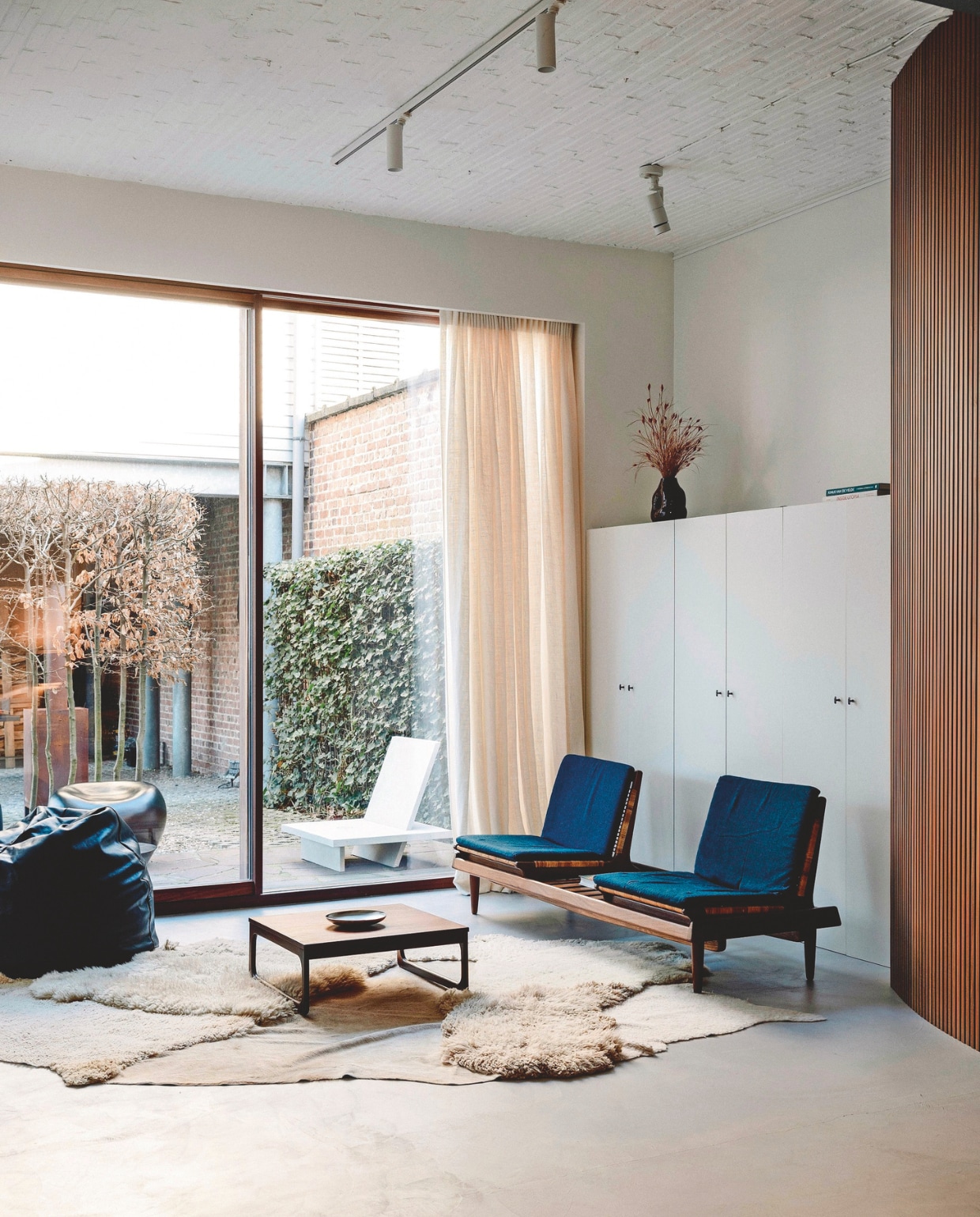 Zoals de meeste meubels heeft Geraldine de houten bank vintage gevonden. De schapenvacht van Carine Boxy geeft de cementvloer meer warmte. Stijlvol Wonen 03-2025 | Fotografie Stie De Neve | Tekst Maya Toebat