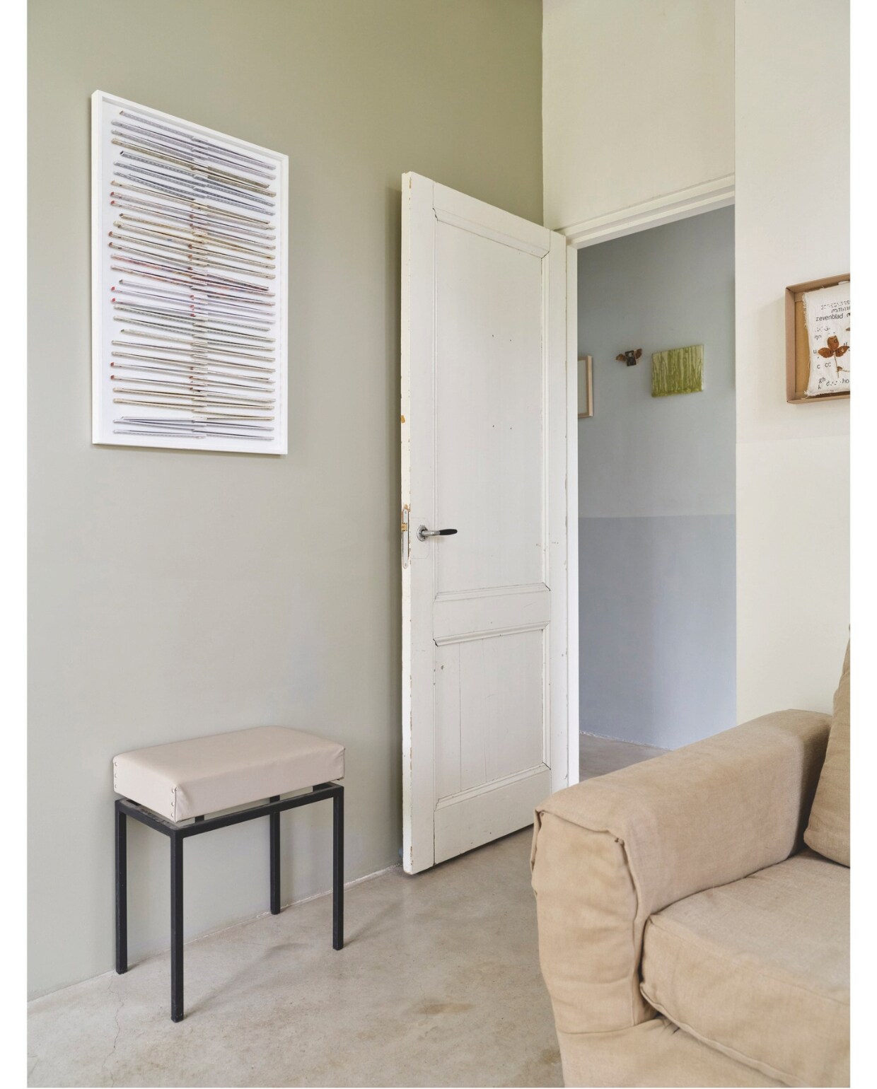 Bank kringloop, bekleed met linnen. Kruk kringloop, gespoten en bekleed met leer. Muurkleur woonkamer Portland Stone Dark, kleur gang Bone China Blue Pale van Little Greene. Kunstwerk woonkamer Ilse Vermeulen, werken  in de gang Ilse Vermeulen en Han Klinkhamer. Vloer gevlinderd beton. vtwonen 03-2025 | fotografie René van der Hulst | tekst Merel van der Lande