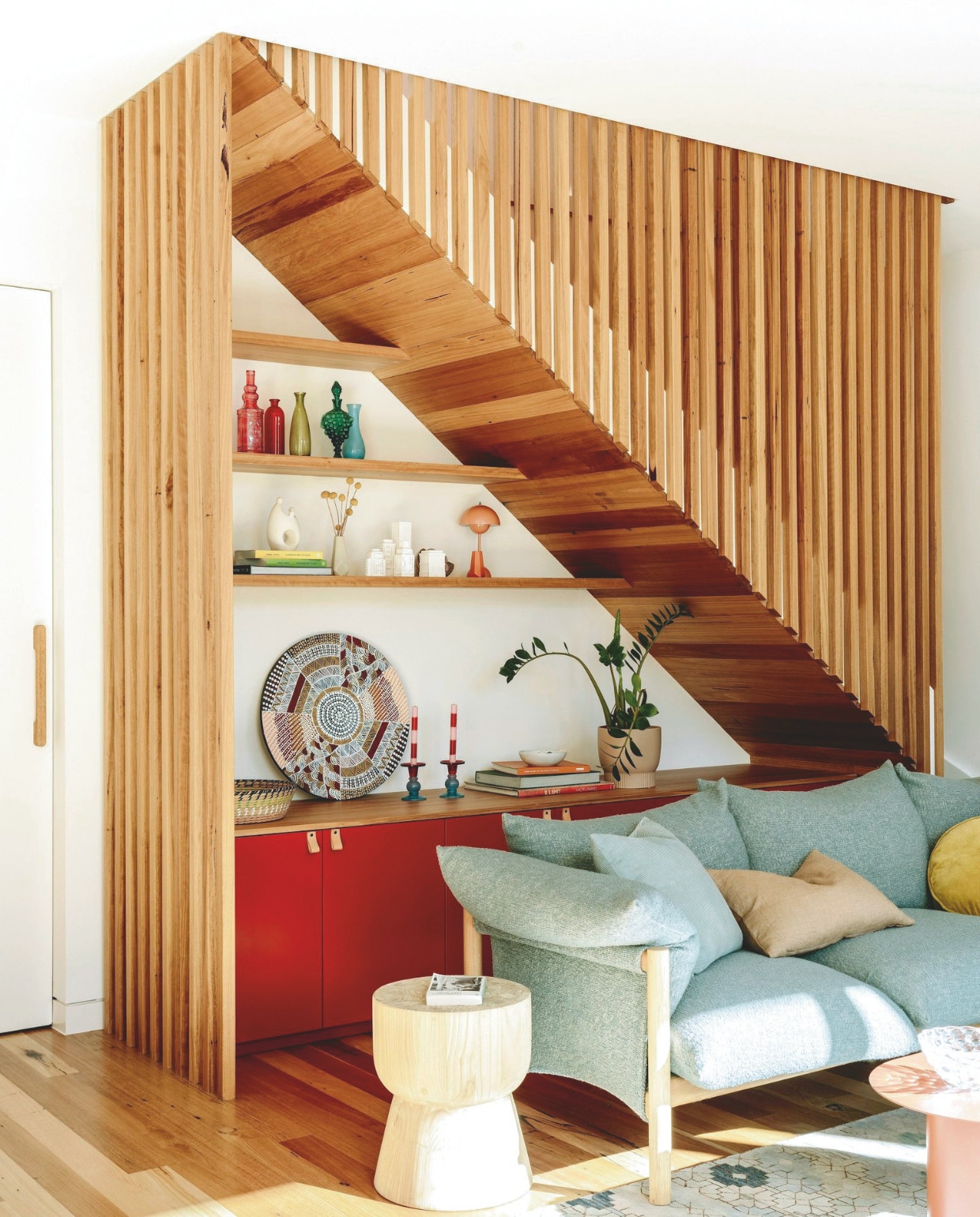 Lattenwand en omlijsting trap van silvertop ash, een Australische houtsoort, ontworpen door Imogen Pullar Architecture, gemaakt door J&amp;RC Builders. Bank Wilfred van Jardan. Vloerkleed Loom Rugs. Muurverf Violet Surprise 6 van Dulux. Kruk Fenton &amp; Fenton. Flessen vintage. Kandelaars Kip&amp;Co. Lamp &amp;Tradition. Rond schilderij Japarra van Russellina Puruntatameri. vtwonen 03-2025 | styling belle hemming | fotografie marnie Hawson | tekst caroline westdijk