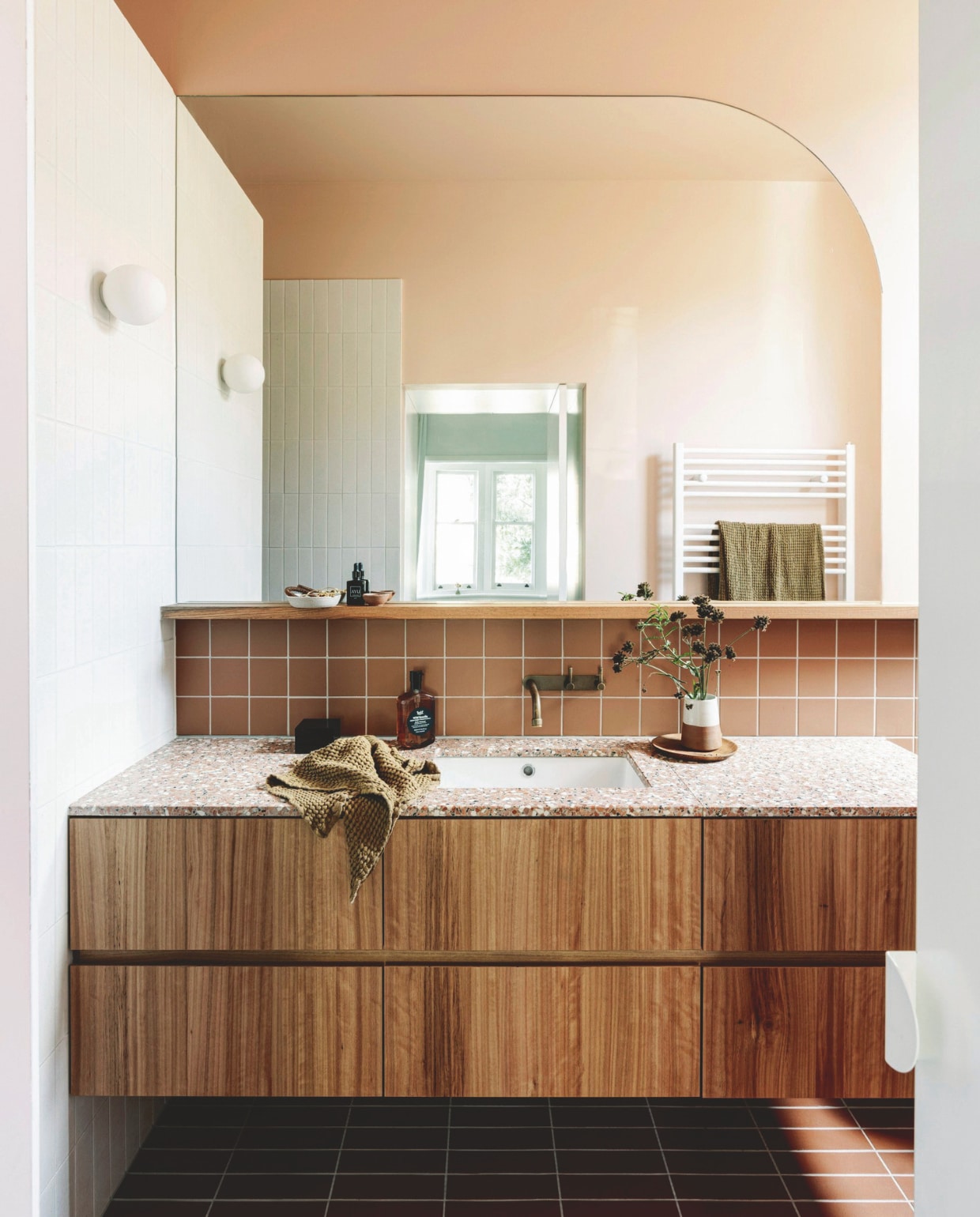 Blackbutt-fineer wastafelmeubel en spiegel ontworpen door Imogen Pullar Architecture, gebouwd door J&amp;RC Builders. Terrazzo blad van Fibonacci. Kraan Brodware. Wandlamp Dioscuri van Artemide. Vloertegels Perini. Muurtegels De Fazio Tiles &amp; Stones. Douchetegels Hida van Academy Tiles. Verf muur en plafond Maiko van Dulux. vtwonen 03-2025 | styling belle hemming | fotografie marnie Hawson | tekst caroline westdijk