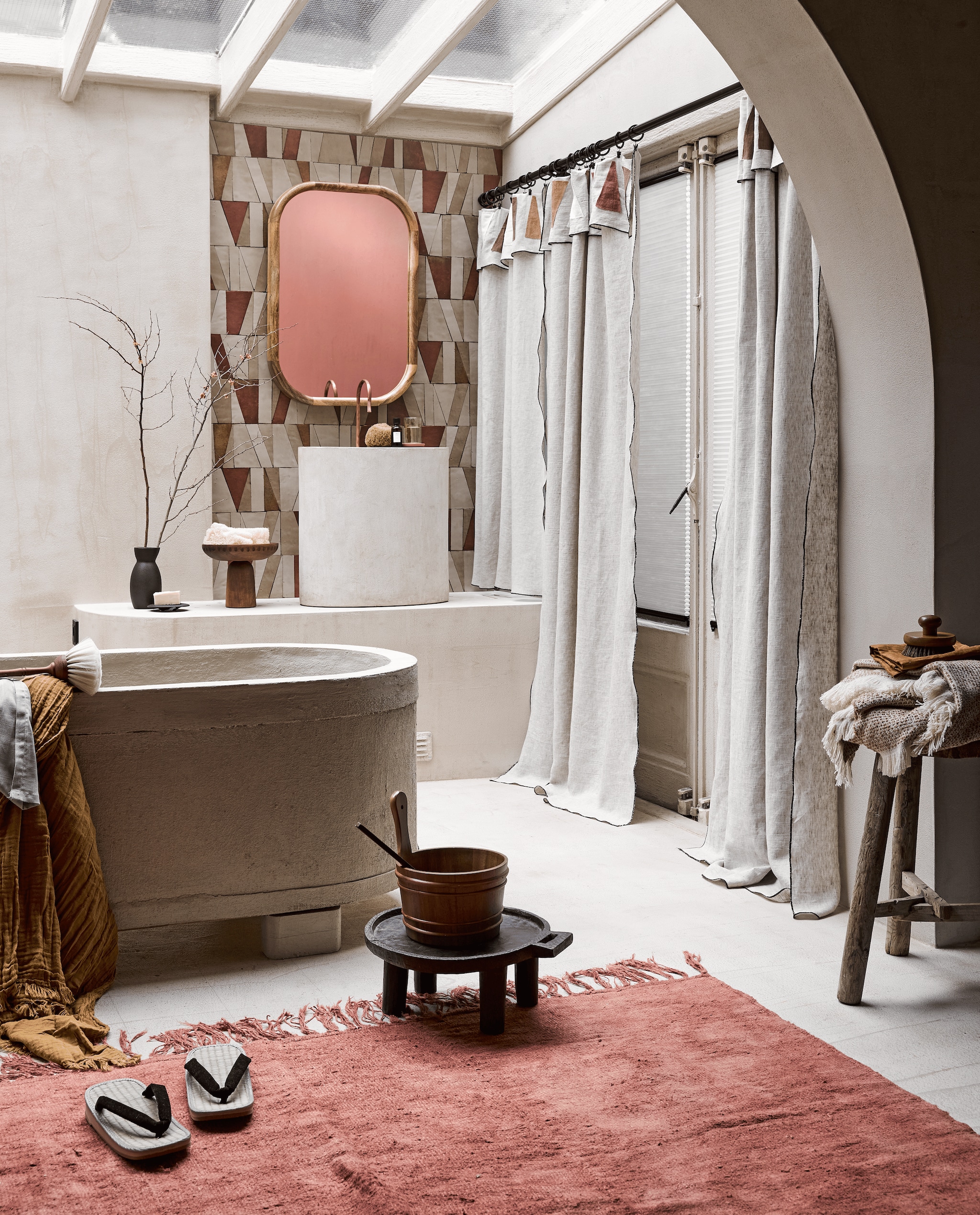 Gordijnen gemaakt door Meta Poulain van linnen gordijnsheets en reststukjes linnen, prijs op aanvraag, borstel op rand van bad, 34 cm (l) € 27,50 (bymolle.com). In de deuren beige verduisterende duettes van Style by Abz, per m² vanaf € 340,- (de-stoffeerder.nl). Behang 03104-245 van Asteré, per rol 70 cm x 10 m € 245,- (loggerewilpower.com). Spons € 8,95, schoteltje waar glazen mok op staat € 6,95 (lanena-home.com). Bad handgemaakt en kraan bij wasbak, prijs op aanvraag (com-anders.nl). Sauna-emmer € 39,99, zwarte vaas, 10×20 cm € 22,99, bijpassend zwart schaaltje € 11,99, borstel op kruk € 15,99, beige plaid met franje, 140×190 cm € 45,99 (zarahome.com). Droogbloemen (plantje.nl). Lepel in houten bak Pure van Serax, 5-delige set € 26,95 (vtwonen.nl). Slippers € 47,60 (japansewinkeltje.nl). Geel plaid, 150×200 cm € 14,99, groene lap stof over bad € 19,99, zwarte gordijnroede uitschuifbaar van 210 cm tot 835 cm € 27,44, zwarte gordijnklemmen, 10 stuks € 3,99 (ikea.nl). Bruine linnen doek op krukje, set van 2 € 7,99, spons bij wasbak prijs op aanvraag (hm.com). Groen glas bij wasbak € 10,-, op zwart schoteltje Aleppo zeep van Mumtaz € 9,-, vintage kleed hennep uit Turkije, 255×177 cm € 990,-, spiegel met houten frame € 271,- antieke kruk rechts € 155,-, Ethiopische koffietafel voor het bad € 105,-(couleurlocale.eu). Houten dienblad op poot € 102,- (homestede.nl). Overig privébezit. vtwonen 03-2022 | styling Liza Wassenaar | fotografie Alexander van Berge