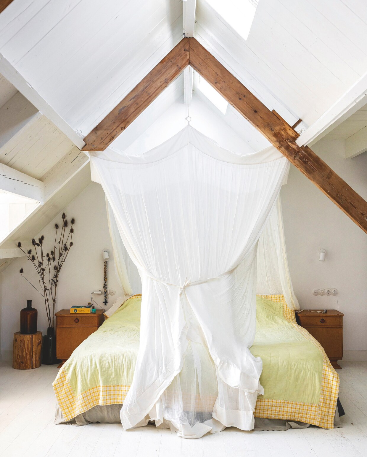 Vloerkleed Ikea. Nachtkastjes vintage uit Polen. Nachtlamp Hue van Philips. Bedhemel zelfgemaakt. Vaas erfstuk. Boomstam uit tuin familie. Muurverf Ral 9010. vtwonen 03-2025 | fotografie margriet hoekstra | tekst adeline mans