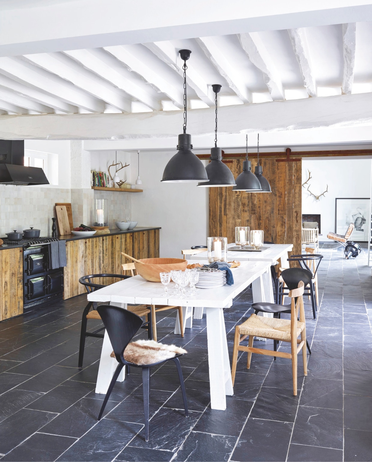 De keuken en schuifdeur zijn maatwerk vanoud eikenhout. Stoelen Carl Hansen en vergelijkbaar Diiiz. Vergelijkbare hanglamp Stoere Lampen. vtwonen landelijk 03-2025 | Productie House of Pictures | Brontekst Ingrid SkaansarStyling José Spaans | Fotografie Sarah Van Hove
