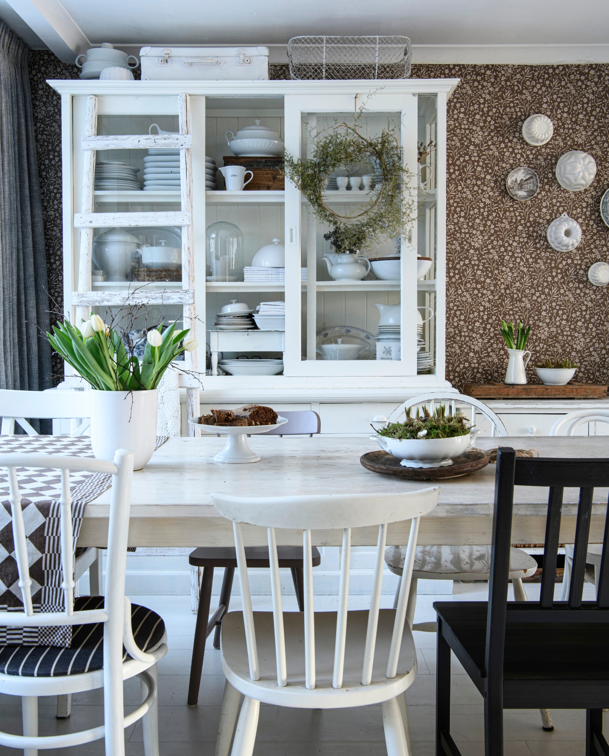 Peggy vond de witte servieskast in een meubelhal. De middelste ruit ontbrak.  Met de hand gemaakte eettafel Marktplaats. Stoelen kringloop. Vloer Capture Eik geverfd Wit van Quick-Step. Gordijnen Kwantum. Behang Estahom vtwonen Landelijk 03-2025 | Styling Janneke Peters, Marit Saladini | Fotografie Louis Lemaire | Tekst Britte Kramer
