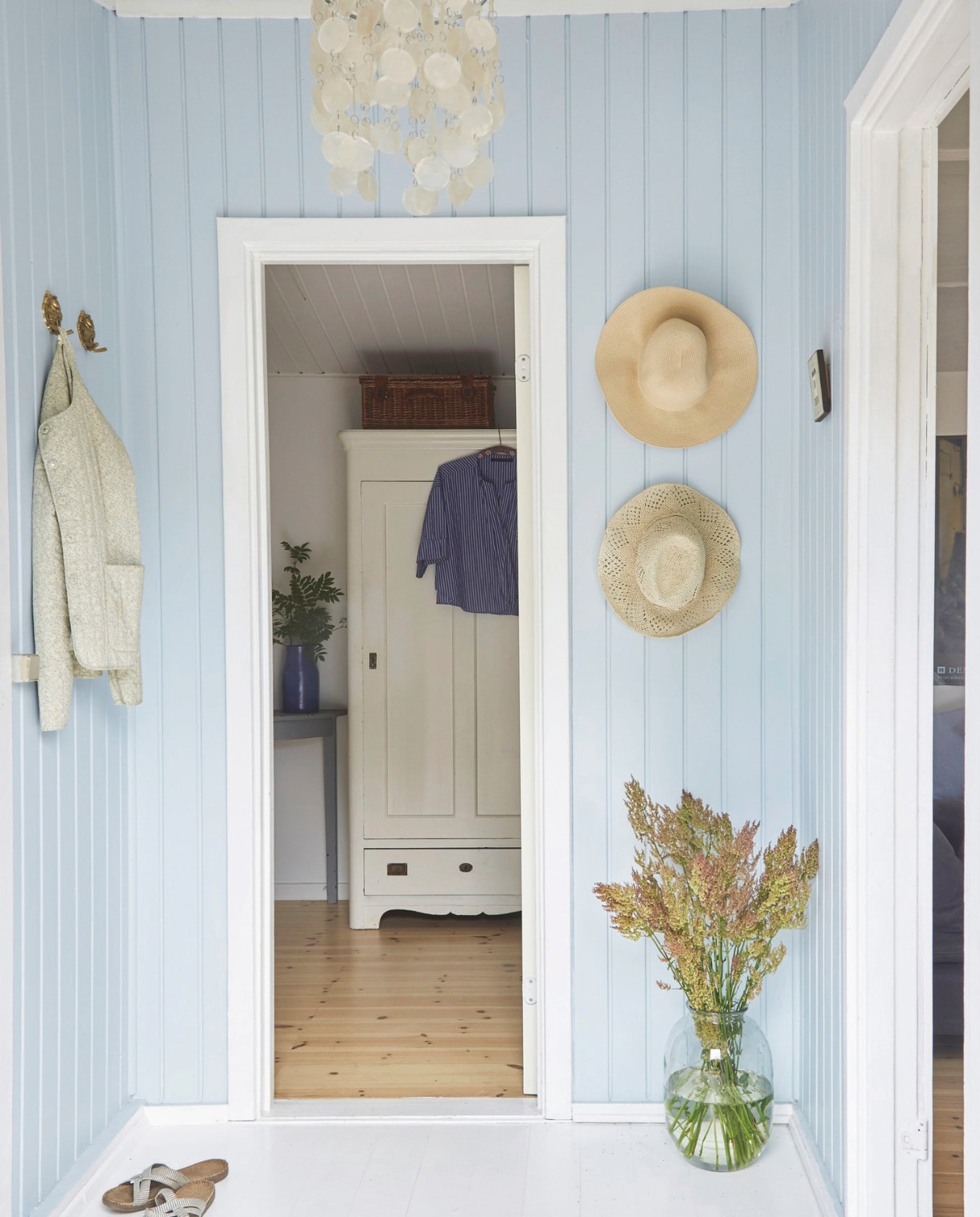 De houten vloer is wit geverfd. Het blauw van de muren mengde Gitte zelf. Rieten hoeden vintage. Soortgelijke lamp metparelmoer schelpen reliving.nl. Deense slippers Shangies bijvoorbeeld bij huushinne.nl. Kast erfstuk van Gittes grootouders. Vaas Tine K Home. vtwonen Landelijk 4-2025 | styling Rikke Graff Juel | fotografie Anitta Behrendt