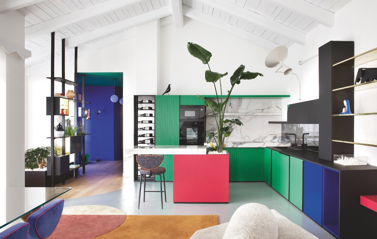 De kleurrijke keuken is een ontwerp van Velvet Studio en bevat een mix van materialen: zwarte fenix, al dan niet geribbelde mdf fronten in de kleuren groen, blauw en rood, gerookt spiegelglas, marmer en messing. Barkruk Muta1 van l’Opificio. Open kast op maat van Velvet Studio. Stijlvol Wonen 04-2025 | fotografie Barbara Corsico | tekst Jackie Oomen | Productie Living Inside / Brontekst Marzia Nicolini