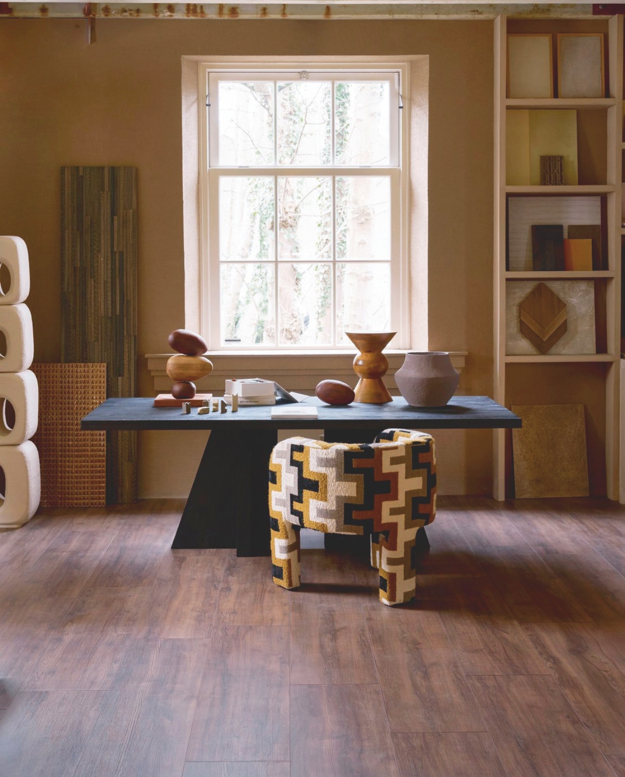 Laminaat XL in Collar Warmbruin, lamel 138x32,6x0,8 cm, met groef, per m² € 32,99.M.m.v. deeekhoorn.nl (eettafel Woood), urbannatureculture.com (kruk op tafel, bruine vaas), rapture.amsterdam (fauteuil), mettesophie.com (houten object), zarahome.com (schaakstukken), dofine.nl (wandafwerking, stalen), hkliving.com (totem), wonderwallstudios.com (houten stalen). Overig privébezit. vtwonen 05-2025 | styling Cleo Scheulderman | fotografie Jeroen van der Spek