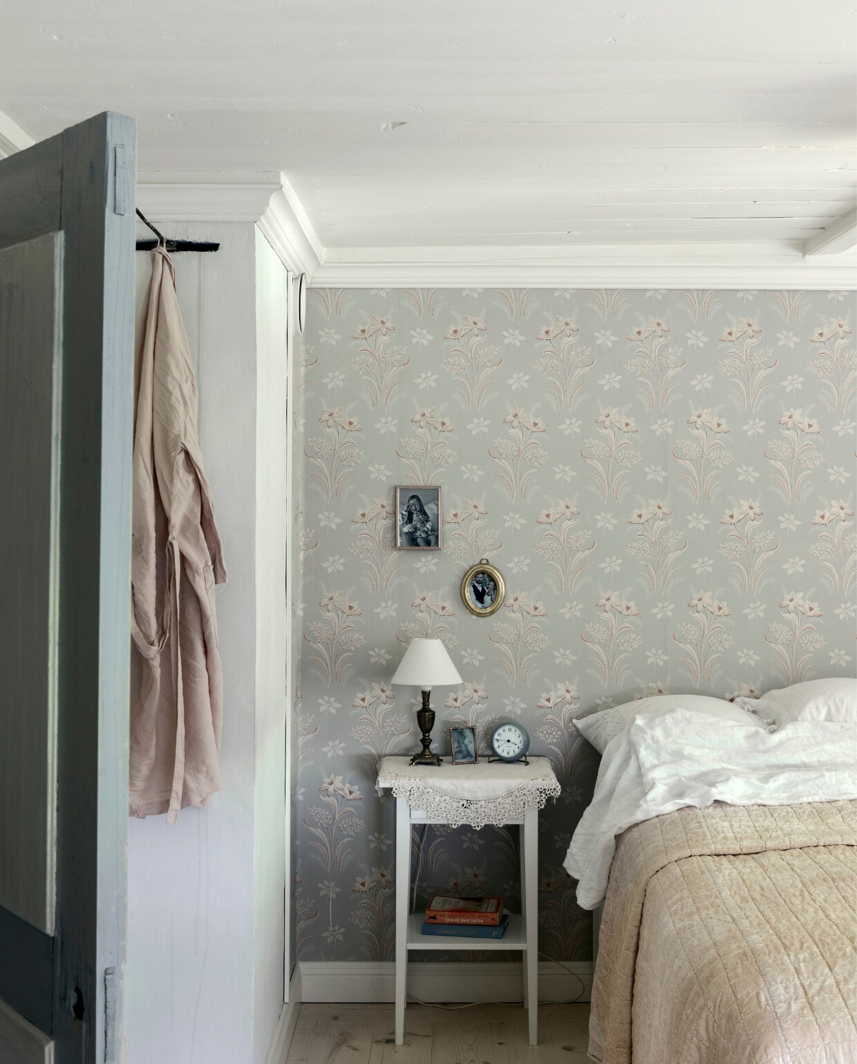 De slaapkamer van Jenny en Tommy straalt rust en sereniteit uit.Het behang ‘Solbacken’ is van Sandberg Wallpaper.Het fijne nachtkastje is van IKEA en gaat al mee sinds Jenny’s studententijd.Het kleine tafellampje was een vondst op de rommelmarkt op het eiland Fagerö.Het mooiste aan deze kamer is de stilte, het licht en het gevoel van verbondenheid met de natuur, door het raam zie en voel je de omhelzing van het groene buitenleven.  vtwonen Landelijk 06-2025 | styling, fotografie & tekst Heikki Rautio | productie Studio Rautio