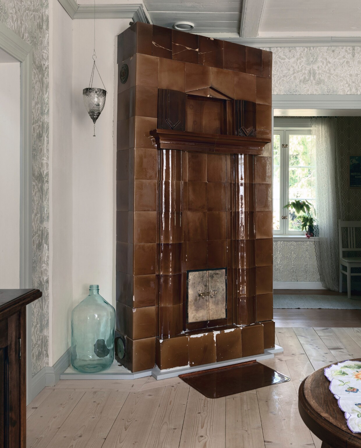 De bruine tegelkachel in de woonkamer dateert van rond 1911. Het huis heeft één tegelkachel en één Högfors-houtkachel, die vooral in de winter worden gebruikt, wanneer het tot -25C kan worden.Het huis heeft tegenwoordig geothermische verwarming en watergedragen vloerverwarming.  vtwonen Landelijk 06-2025 | styling, fotografie & tekst Heikki Rautio | productie Studio Rautio